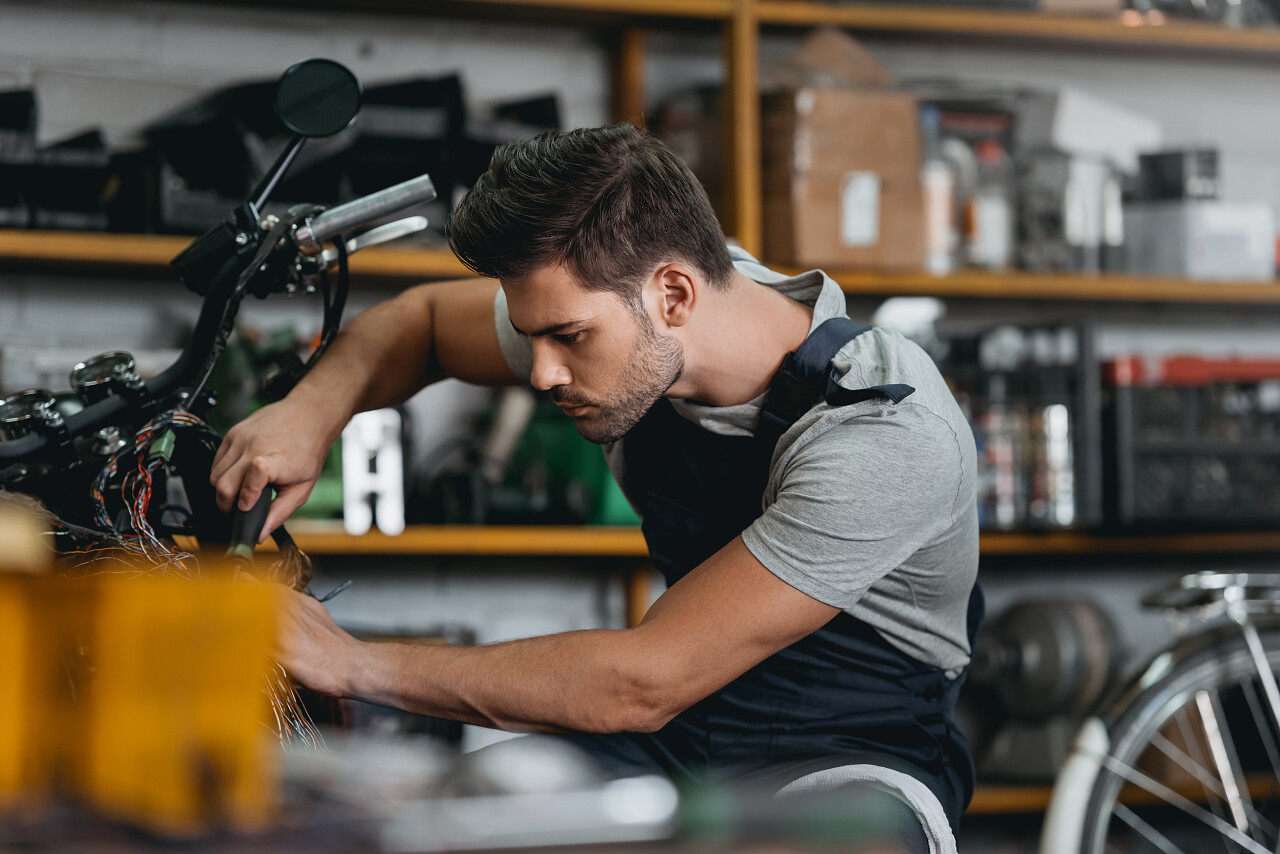 年轻英俊技工戴着护目镜在车间维修摩托车