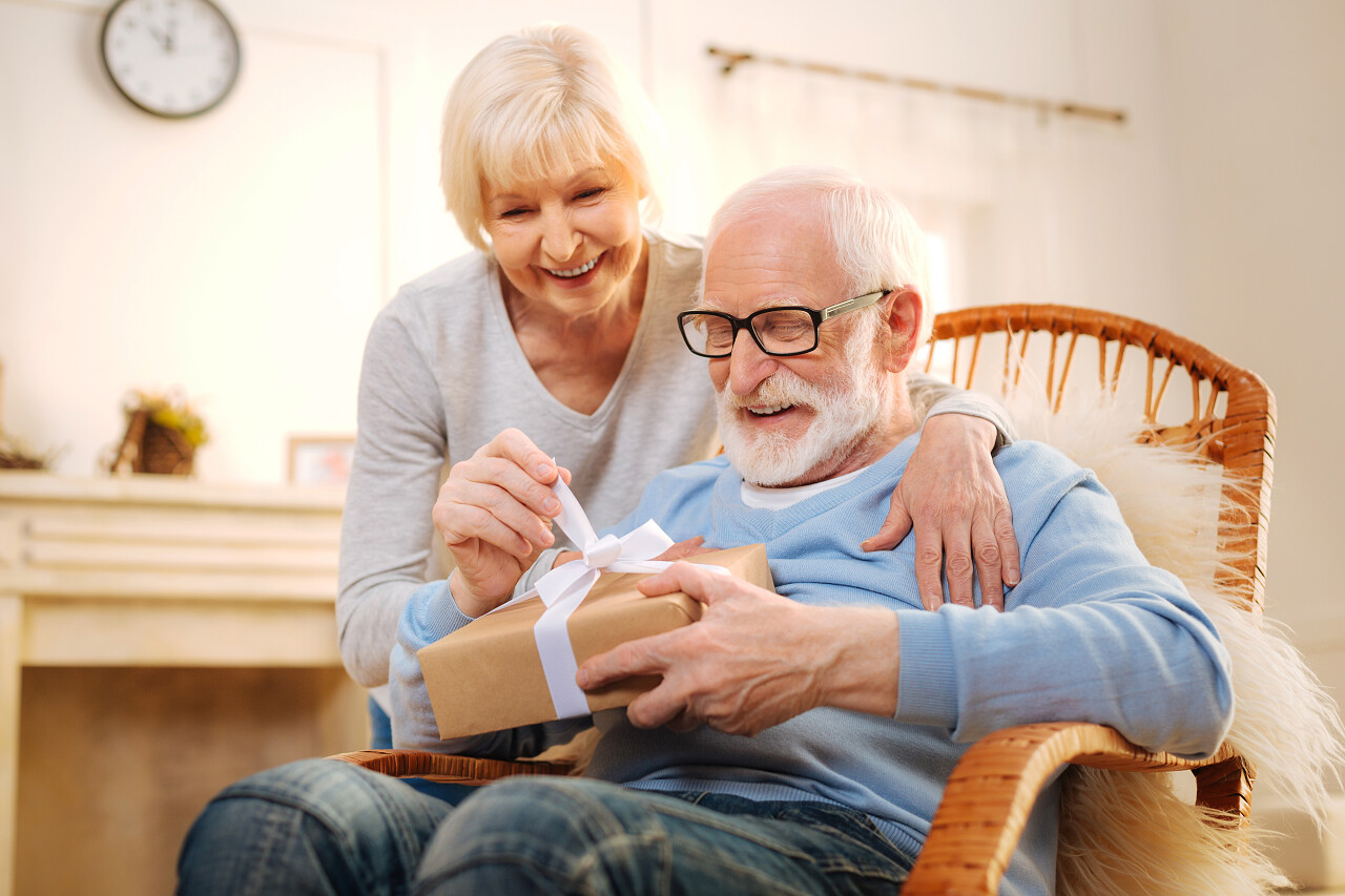 年老的夫妻坐在舒适的椅子上拆礼物放松感动