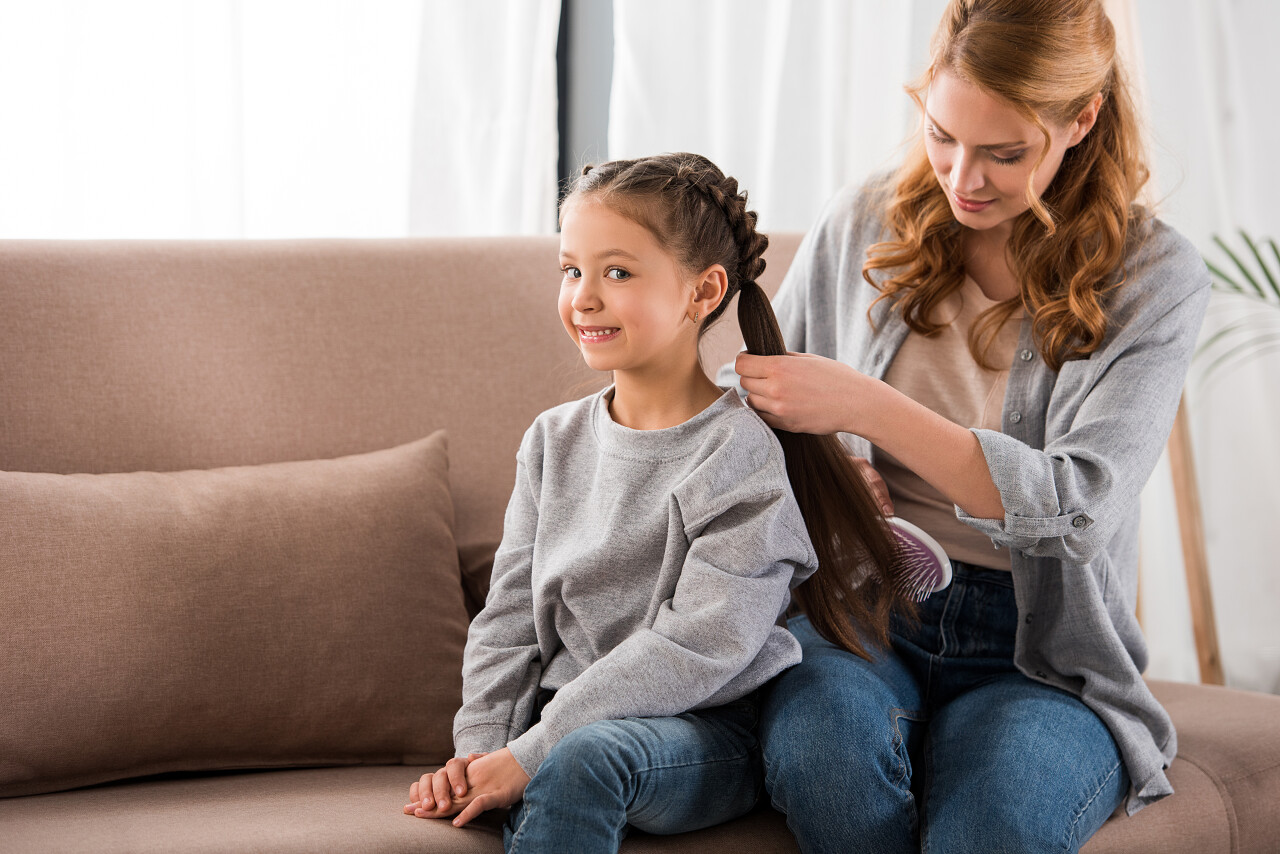 妈妈在家里刷头发可爱的微笑的小女儿