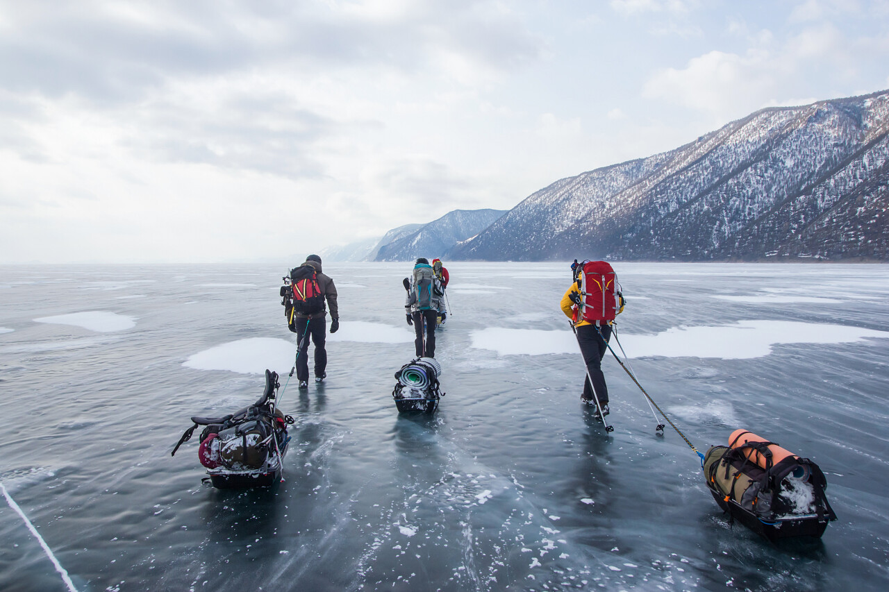 三人背着背包穿过冰水表面和山上的背景俄罗斯贝加尔湖