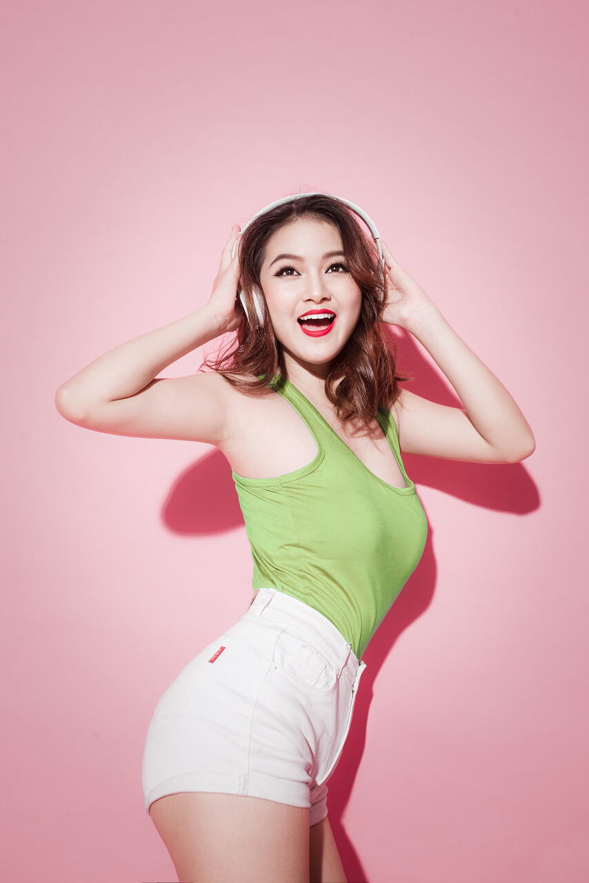 生活方式俏丽的亚洲女孩有乐趣在粉红色与耳机跳舞和唱歌.