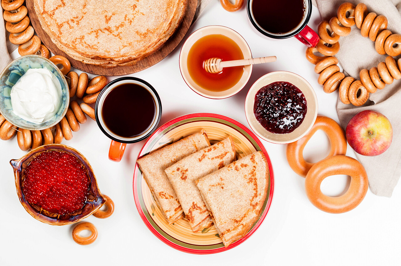 俄罗斯煎饼与覆盆子果酱蜂蜜新鲜奶油和红色鱼子酱白色背景