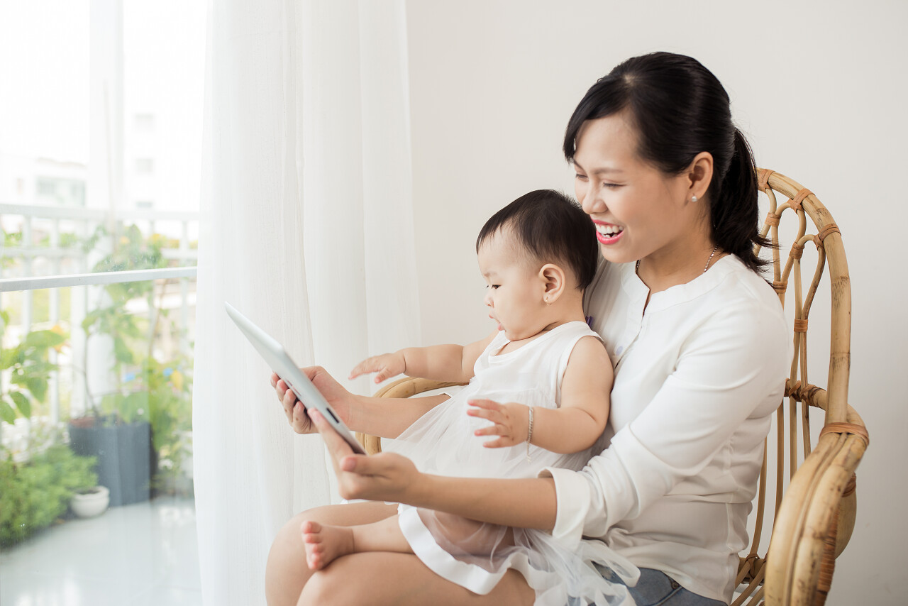 快乐亚洲妈妈和宝宝在家中白色房间窗户附近一起玩乐的肖像月嫂