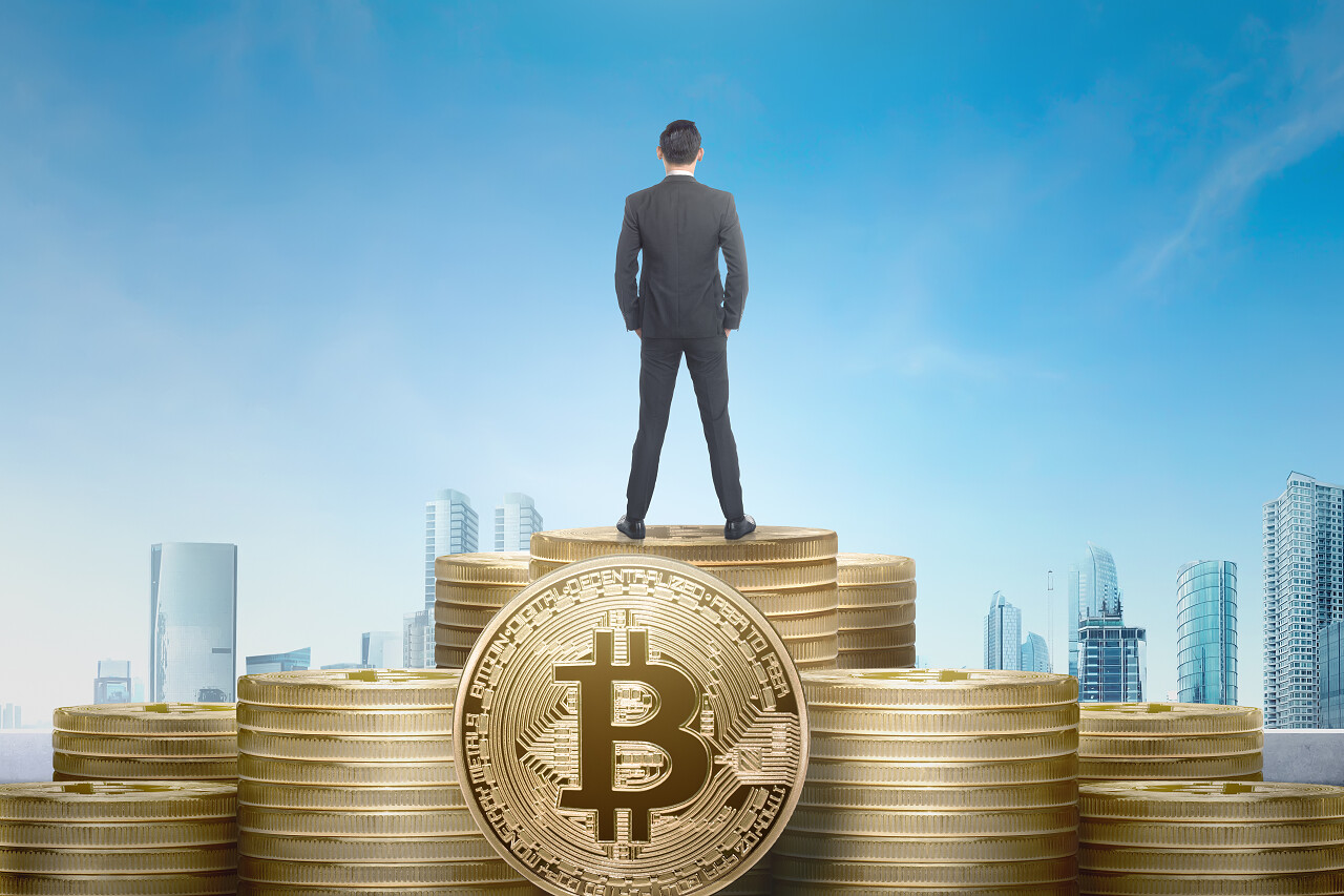 亚洲商人站在具有城市背景的比特币栈上