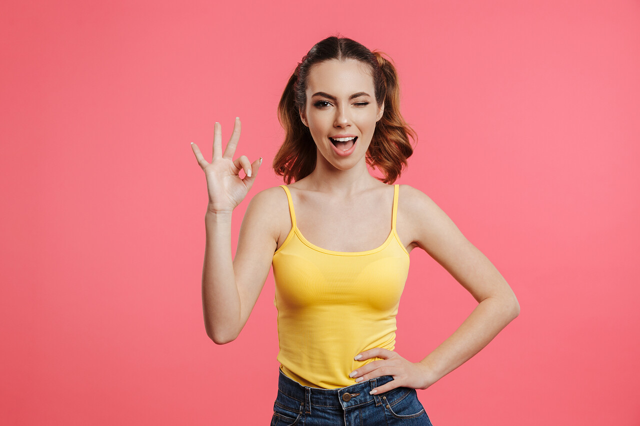 一个满意的年轻女孩的肖像穿着夏天的衣服显示手势