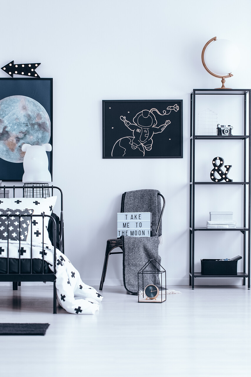 黑色宇航员上的白色墙壁上的椅子上与毯子旁边的床和书架在孩子的卧室