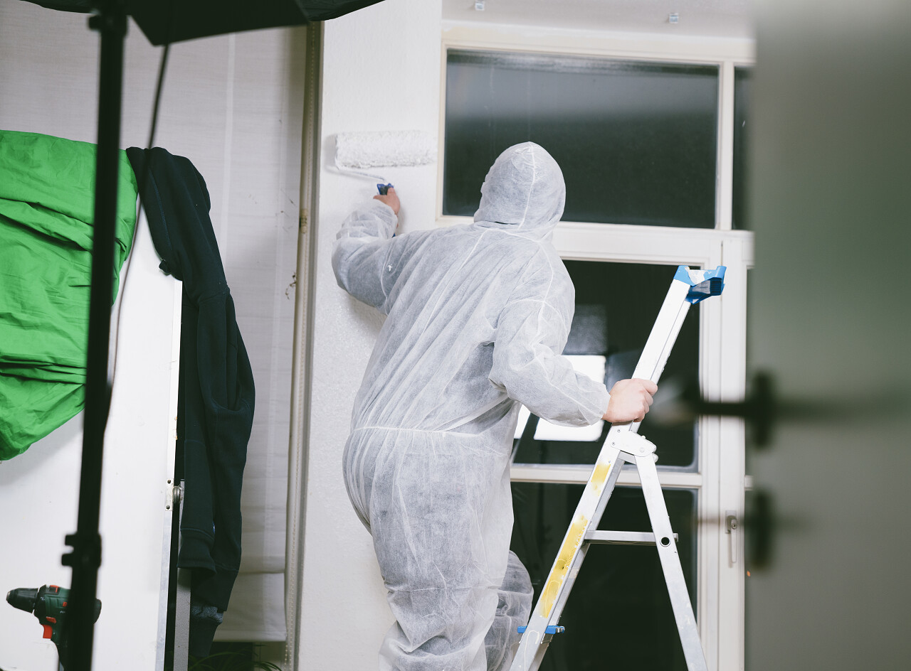 画家使用油漆滚筒和刷油漆房间在白颜色的特写