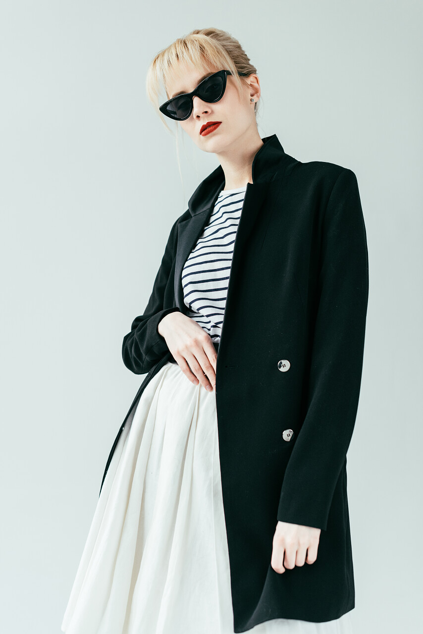 时尚的金发女孩身穿黑色夹克和太阳镜隔离灰色