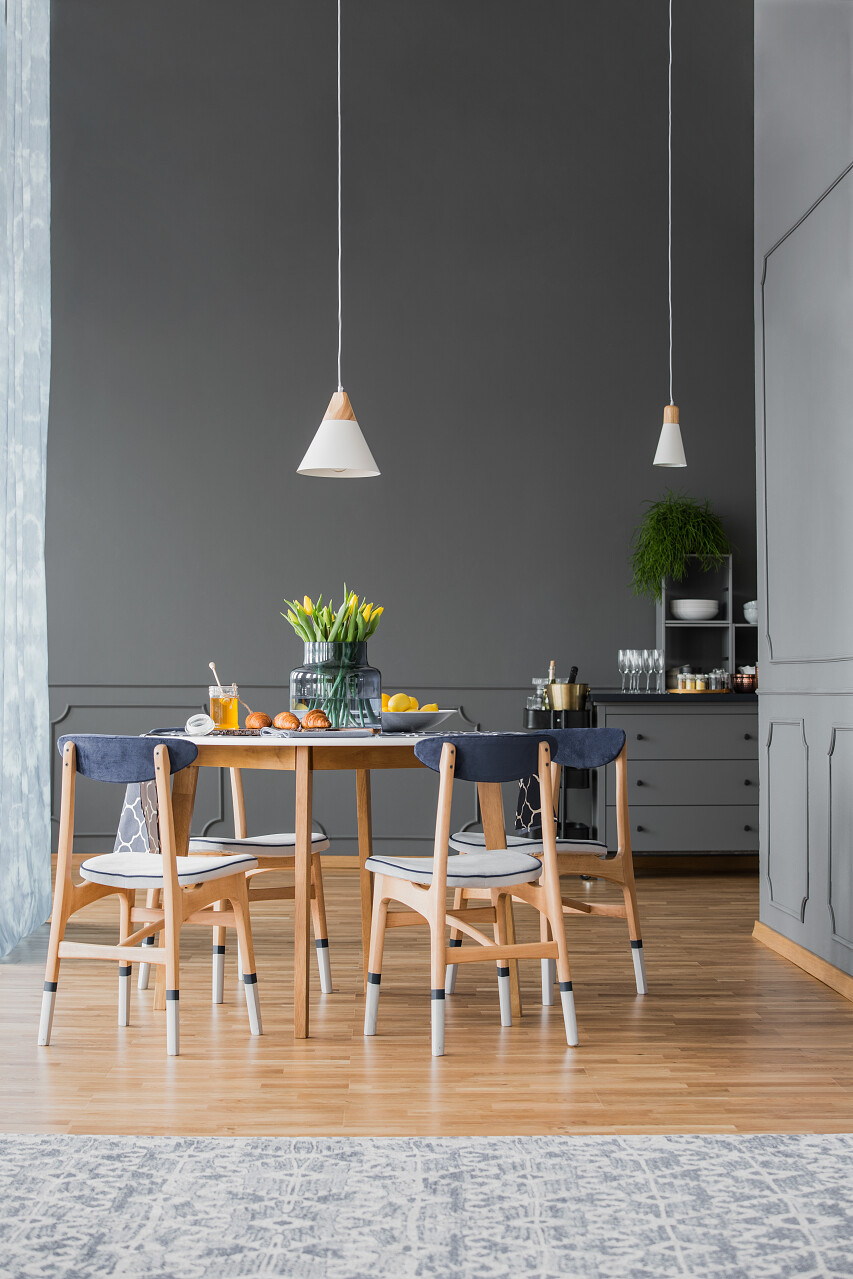 低挂坠灯以上的小木制厨房桌子上的花朵在单色餐厅内部与造型在高大的灰色墙壁上