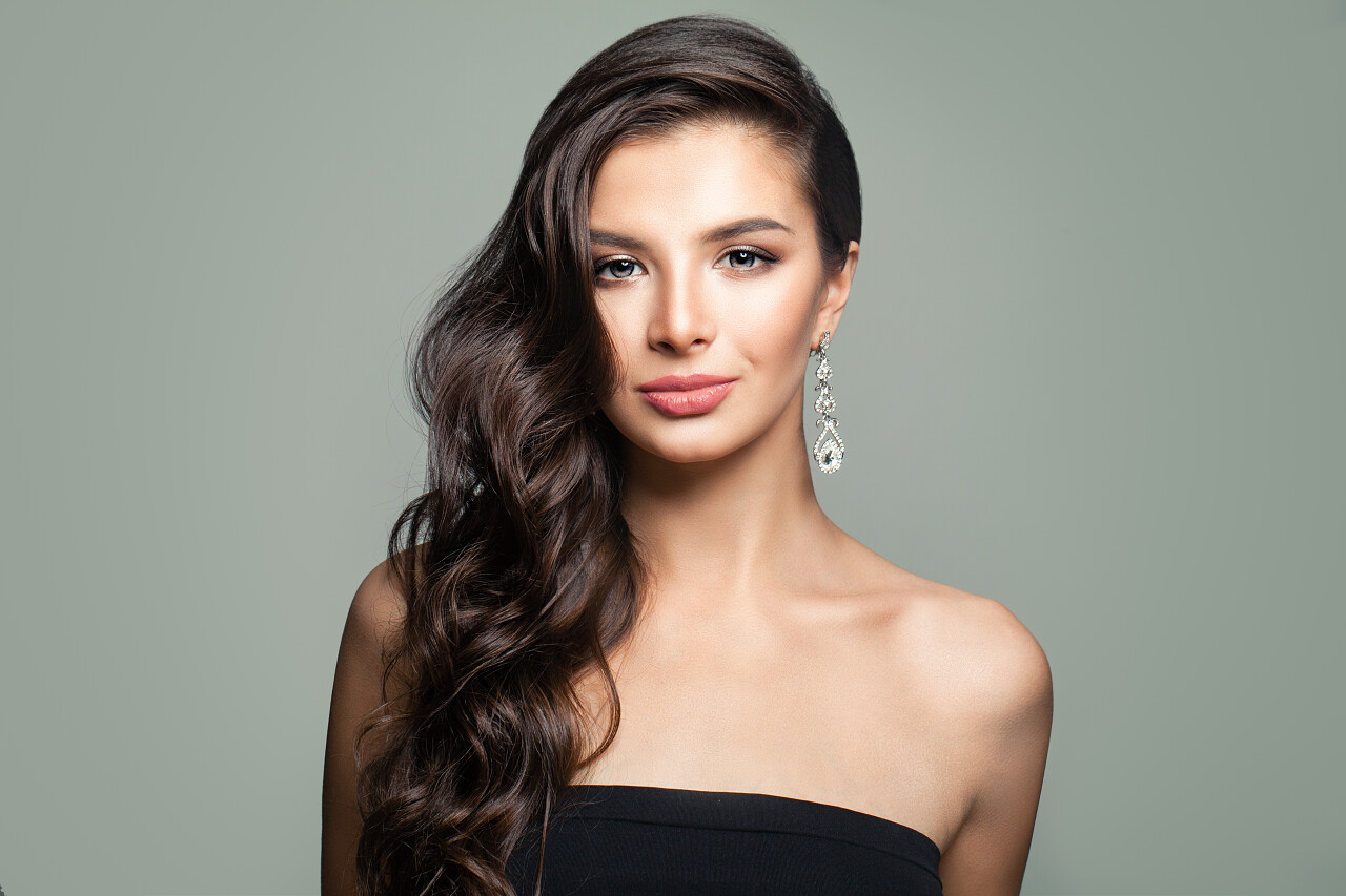 美丽的黑发妇女与长卷曲头发灰色背景。可爱的女性面孔女生头发长头发美女