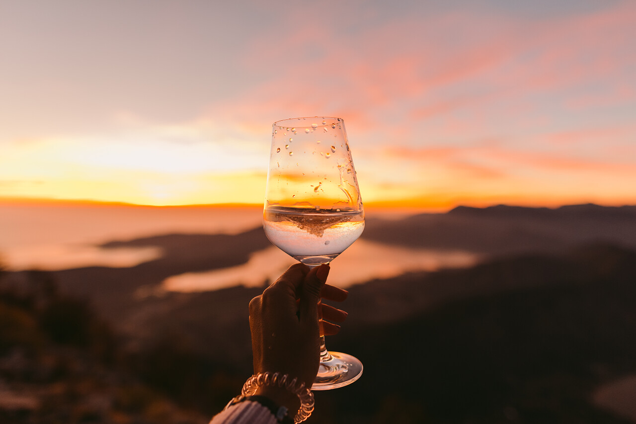 在夕阳下妇女拿着一杯白葡萄酒
