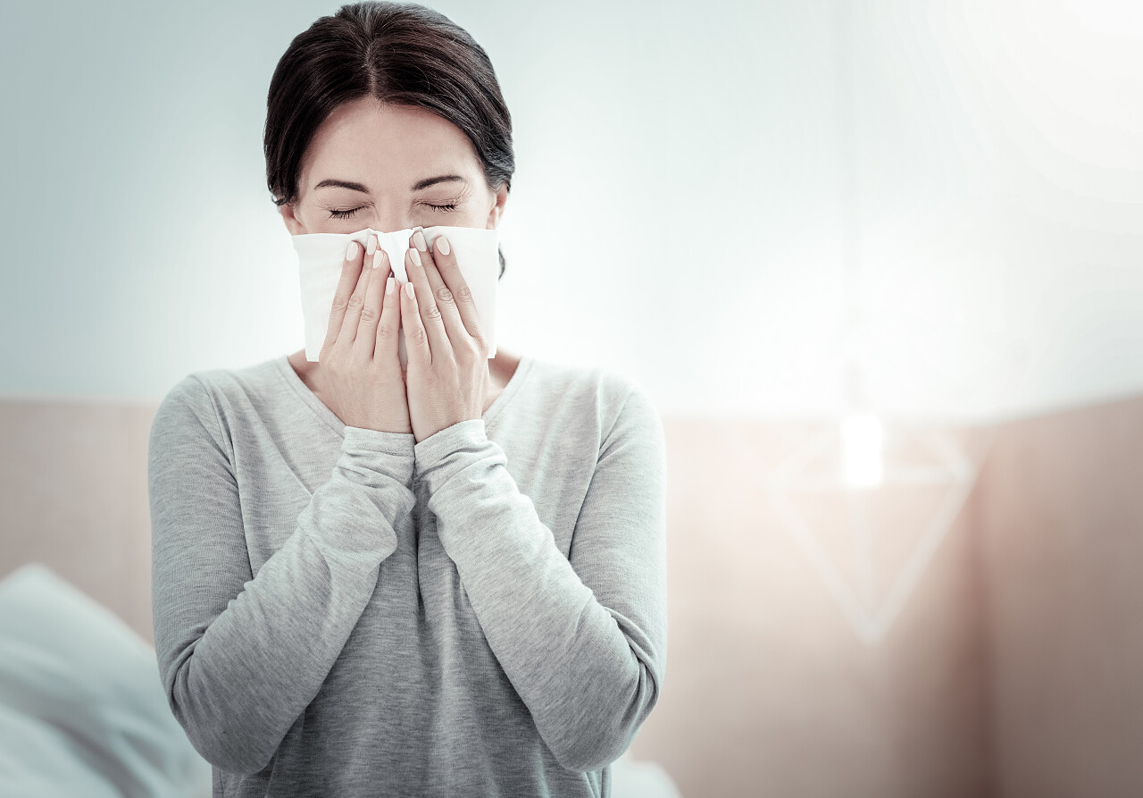 疲惫的生病的女人坐在卧室闭上眼睛打喷嚏