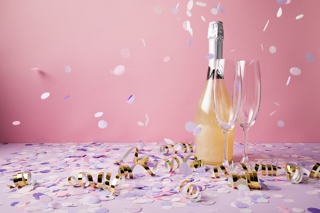 一瓶香槟和玻璃杯在紫罗兰表面上掉落着纸屑片