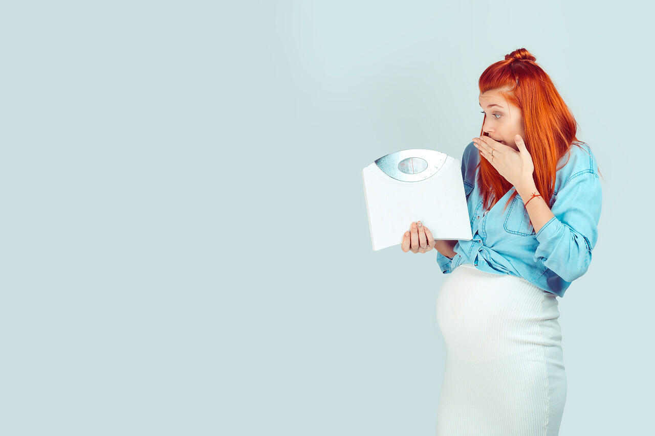 年轻的红头发女人期待婴儿和看体重秤与恐惧