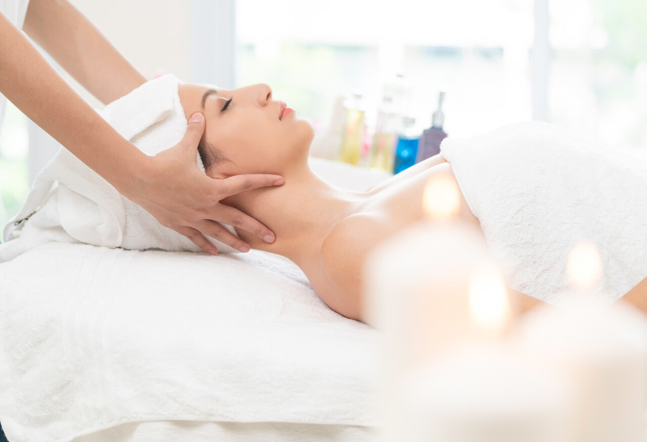 妇女躺在床上接受按摩治疗师的面部和头部按摩治疗放松面部清洁脸部面部按摩中医养生头部按摩