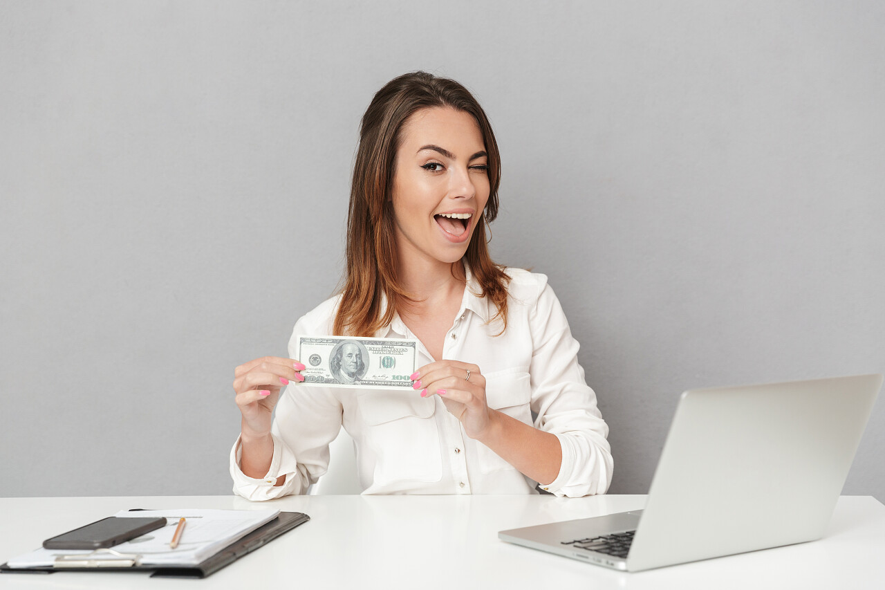 一个年轻的商务女性举着钞票坐在办公桌前