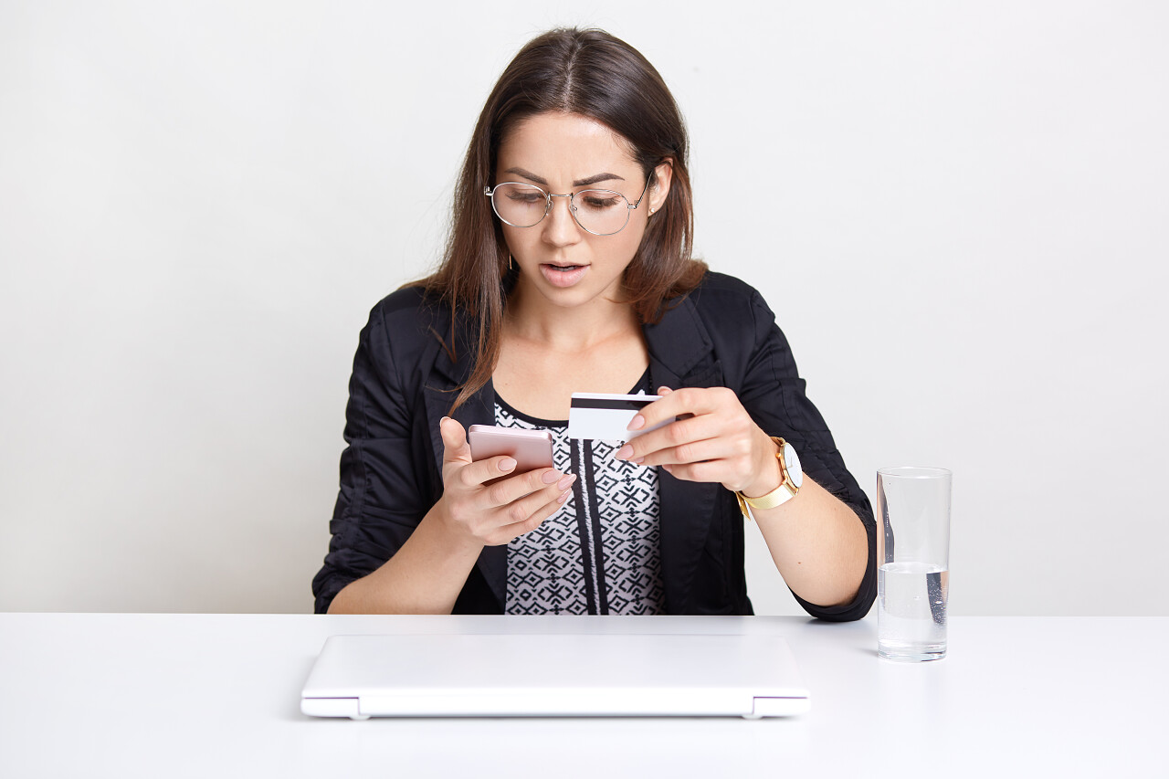 困惑的年轻女性手拿银行卡看着手机震惊