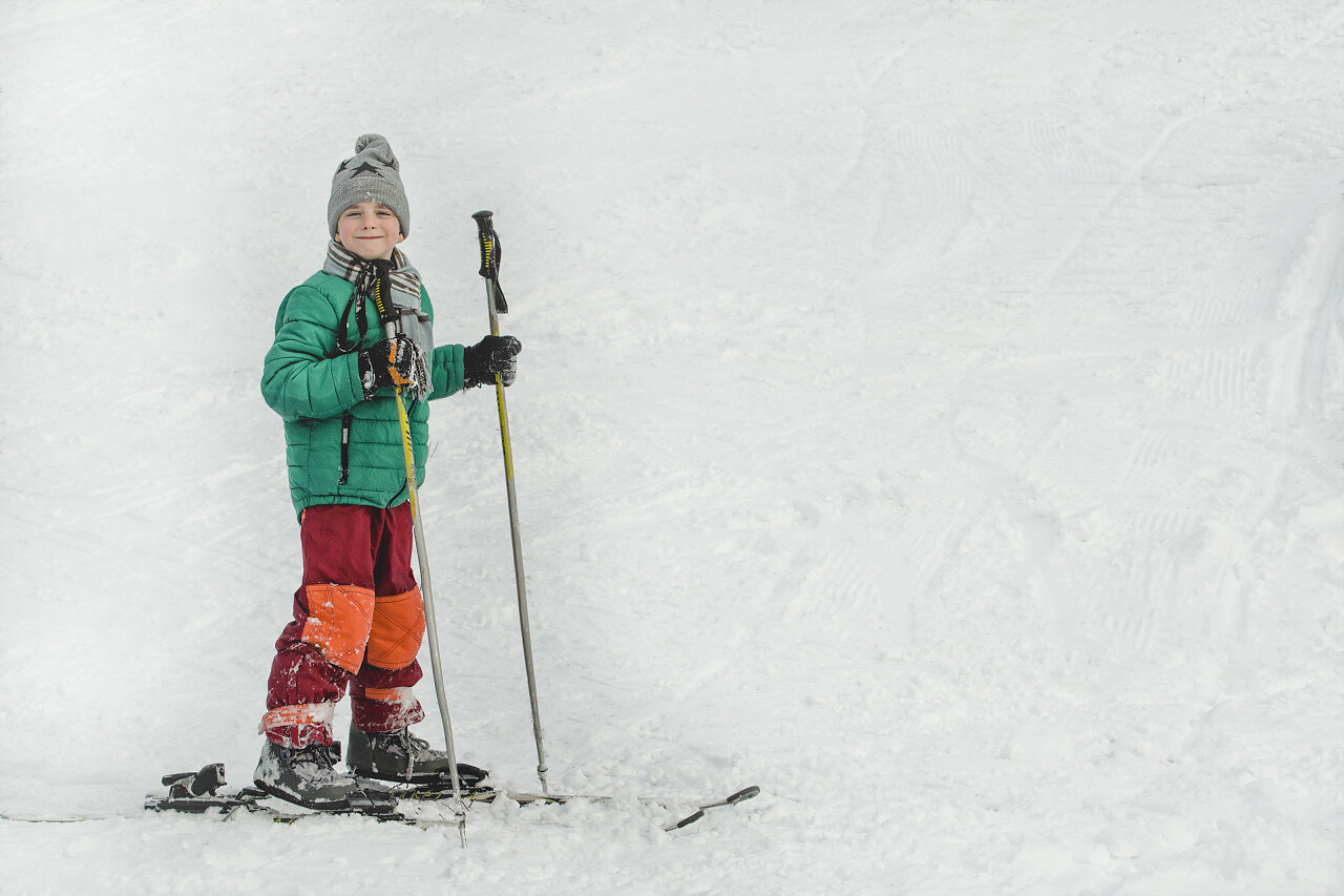 拿着滑雪杆站在滑雪板上的男孩笑了