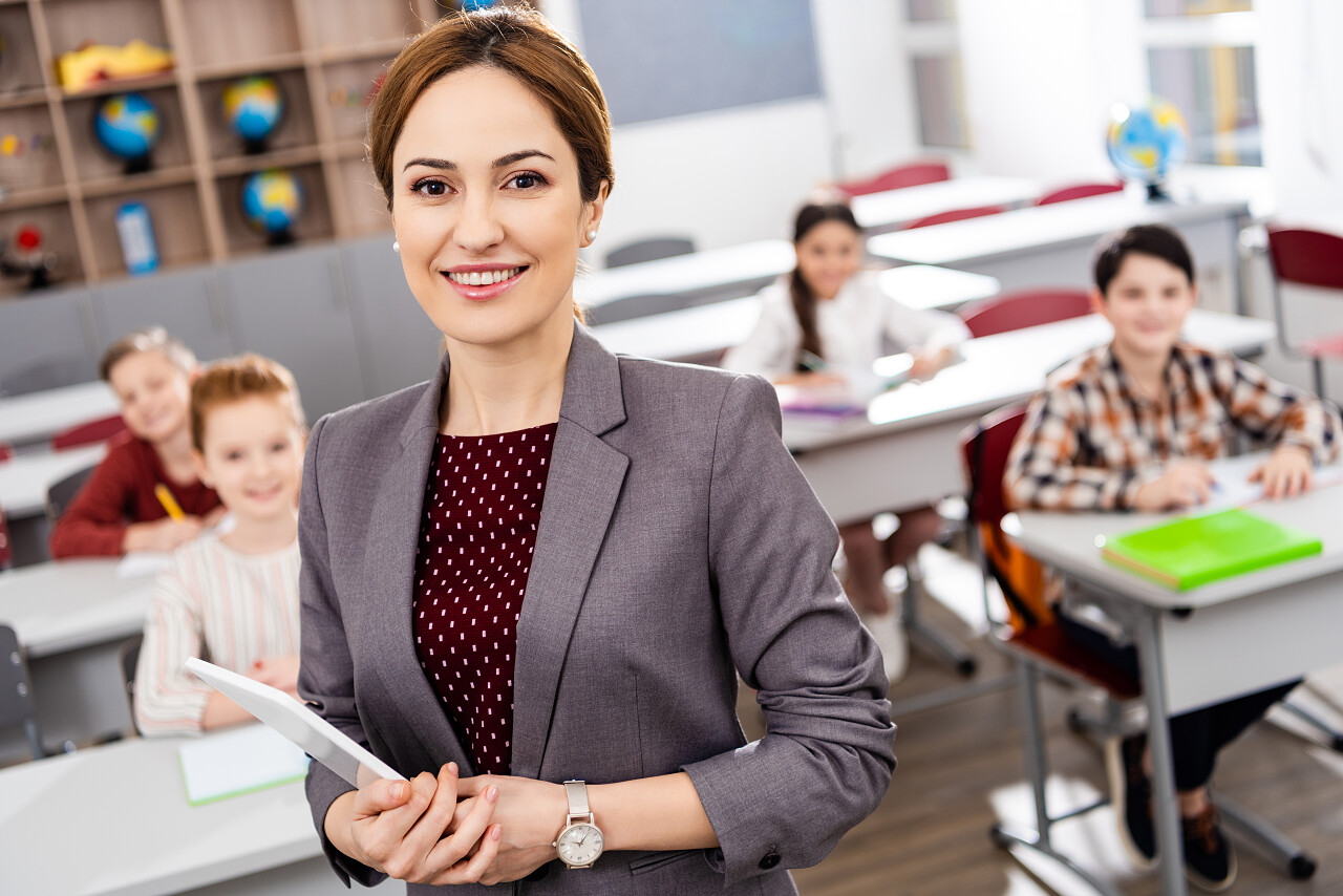 微笑的老师拿着数字平板电脑站在学生面前