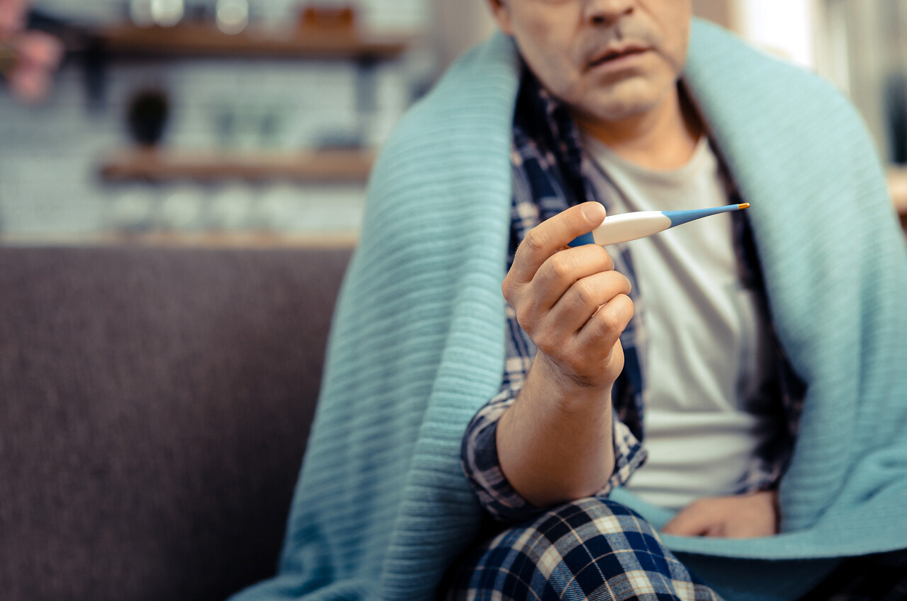 一个生病的男人拿着手里的温度计测温