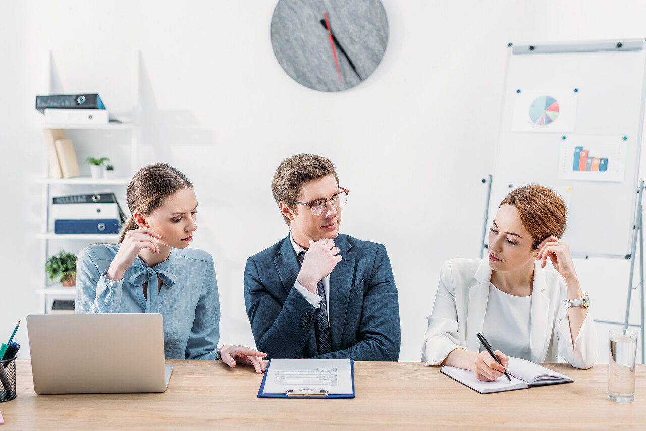 沉思的招聘人员在眼镜看同事拿着笔在笔记本附近