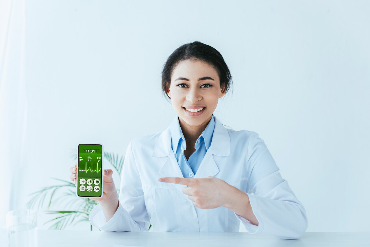美丽的医生指着智能手机与心跳率在屏幕上心跳率应用程序