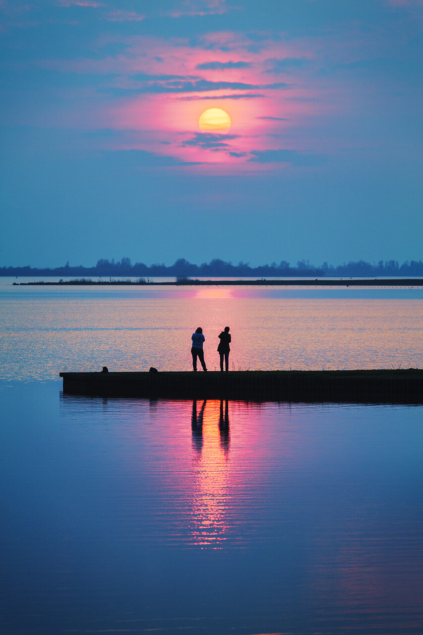 浪漫的日落与人们在湖边的码头一起观看日落在一个多彩和温暖的夏天的夜晚