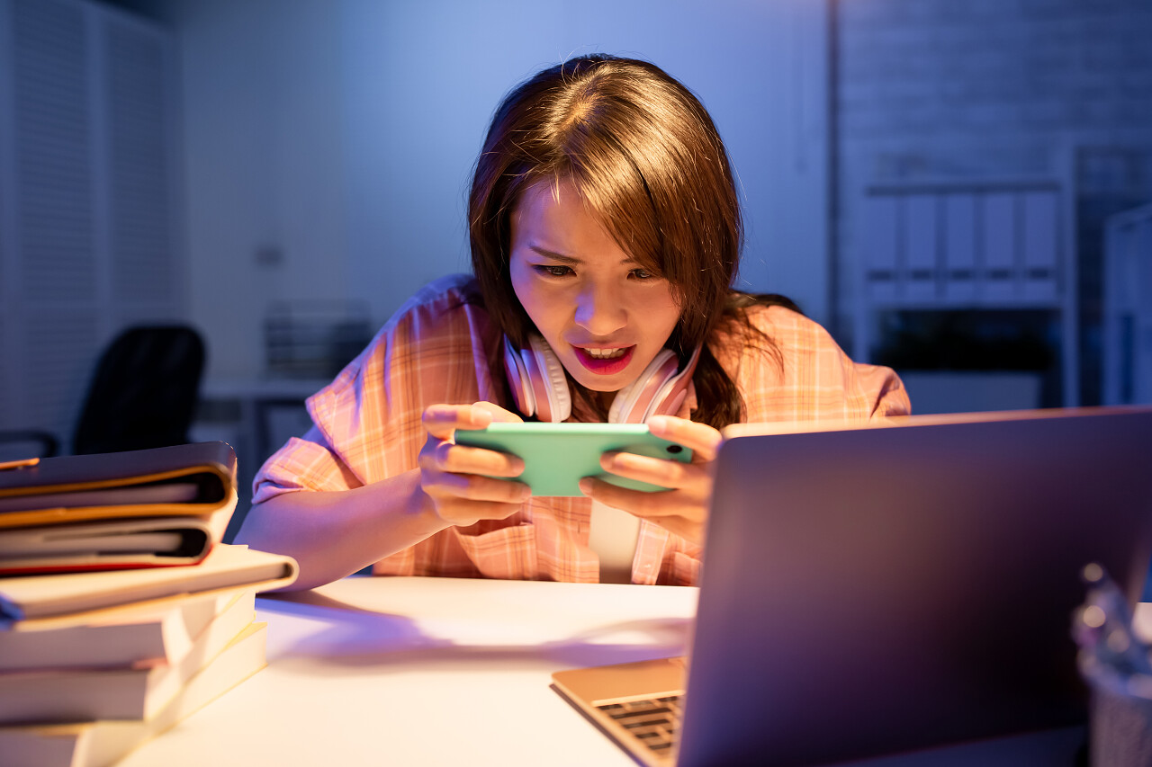 亚洲学生在晚上的智能手机上玩游戏