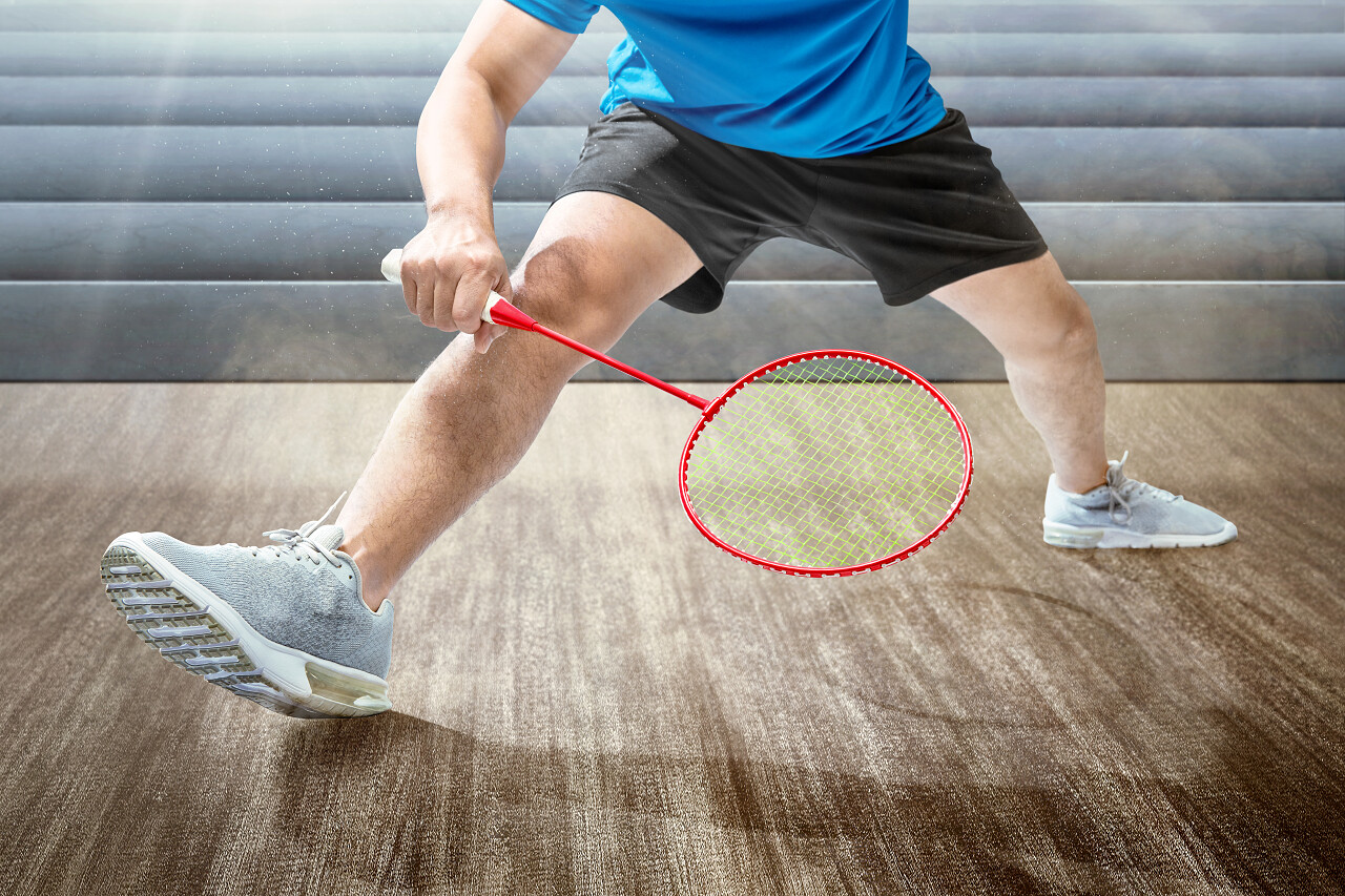 男子在室内球场上用羽毛球拍打羽毛球