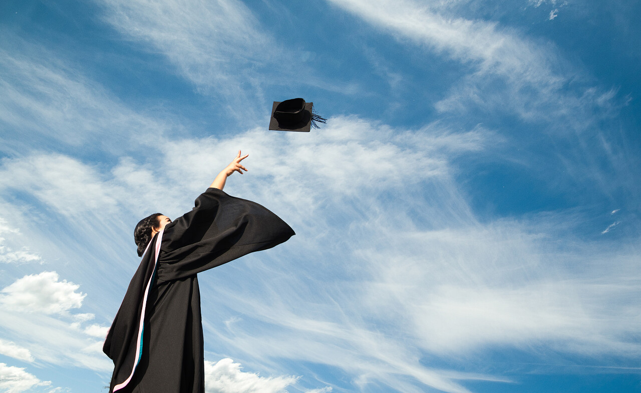一个毕业生在毕业典礼上把一顶帽子抛向天空