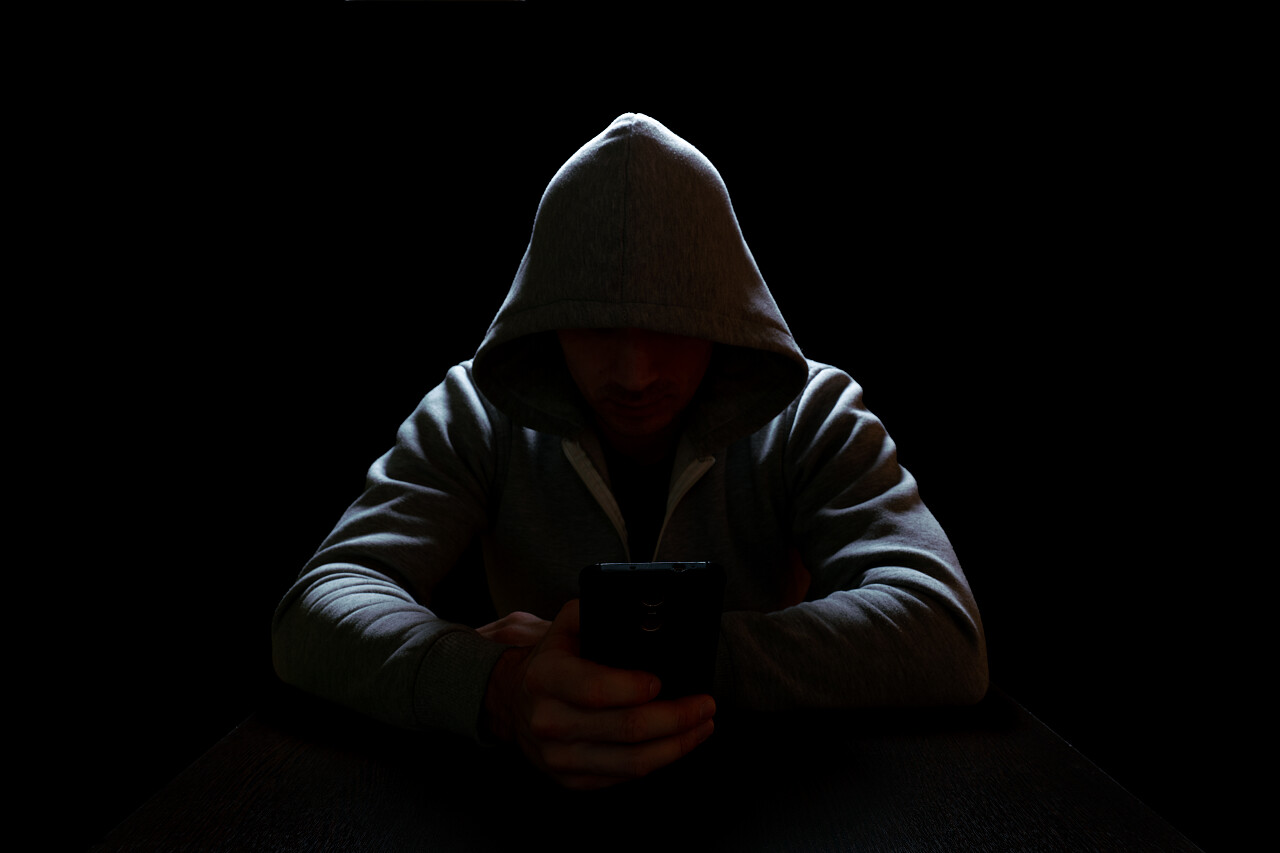 电话欺诈者坐在桌子边的黑暗中手里拿着一部电话