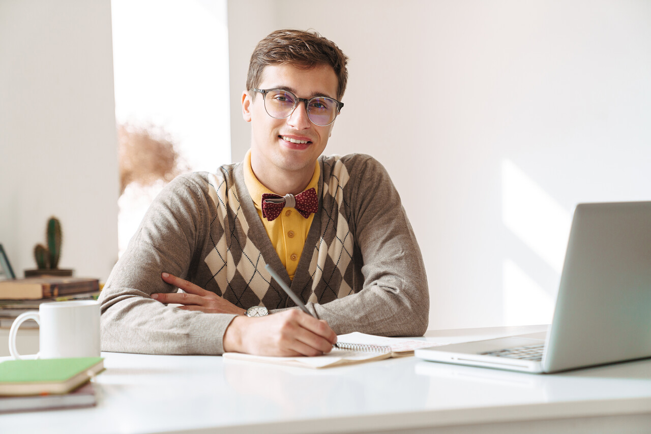 一个快乐的积极向上的年轻人坐在桌旁在屋里写作业