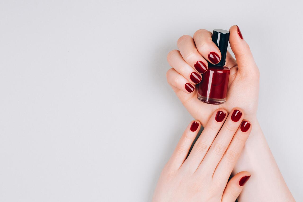 漂亮的深红色美发与一瓶指甲油在灰色背景的手