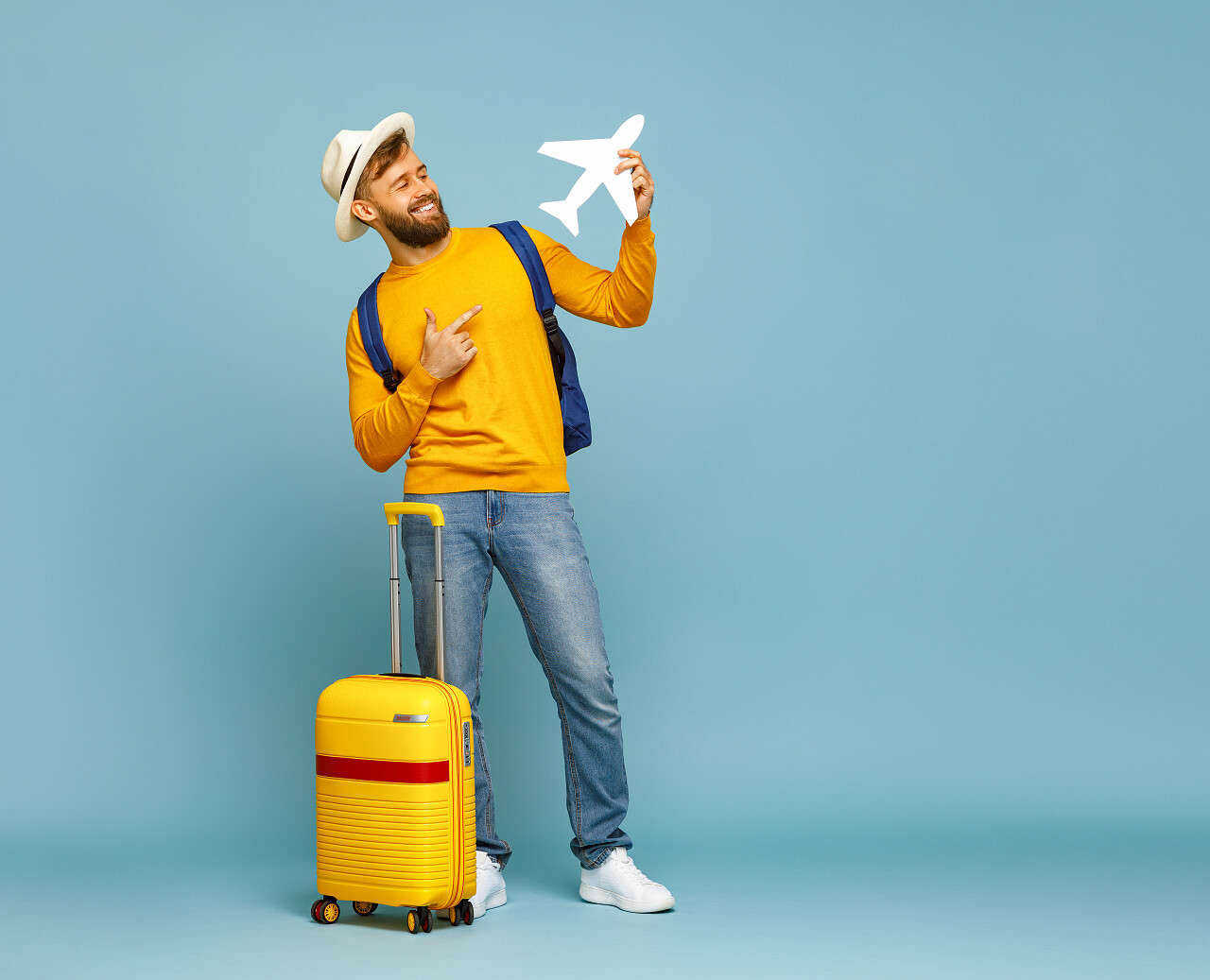 蓝色纯色背景男人笑着指着玩具飞机行李旁边