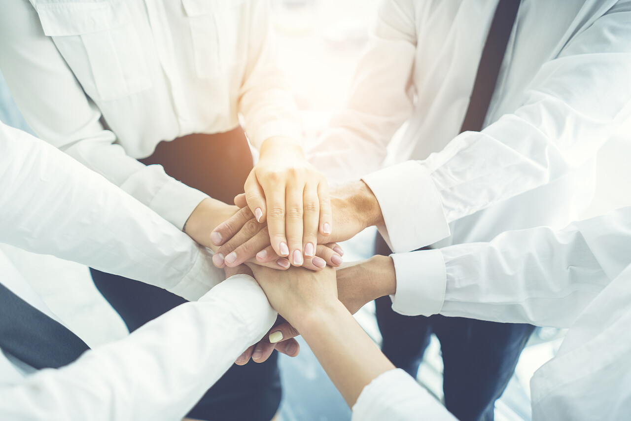 商人们在阳光灿烂的背景下手拉手团队加油团结手势