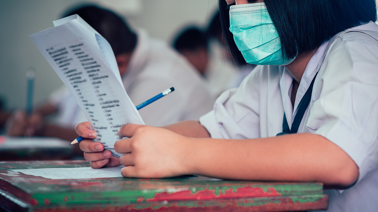 戴口罩保护的学生以及在学校教室里做试卷练习的学生