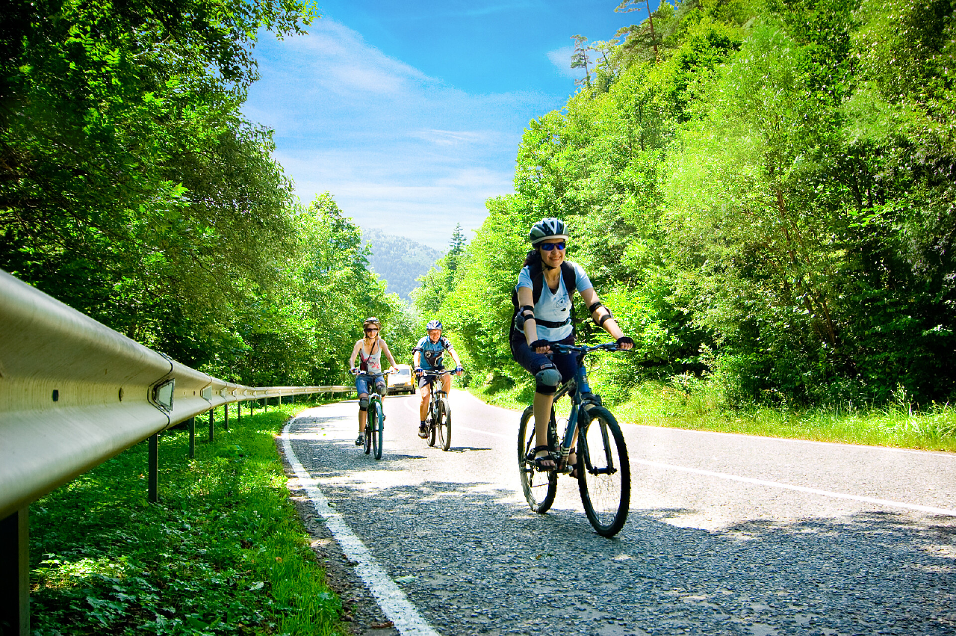 蓝色天空下在森林道路上骑自行车的三个人骑自行车的人