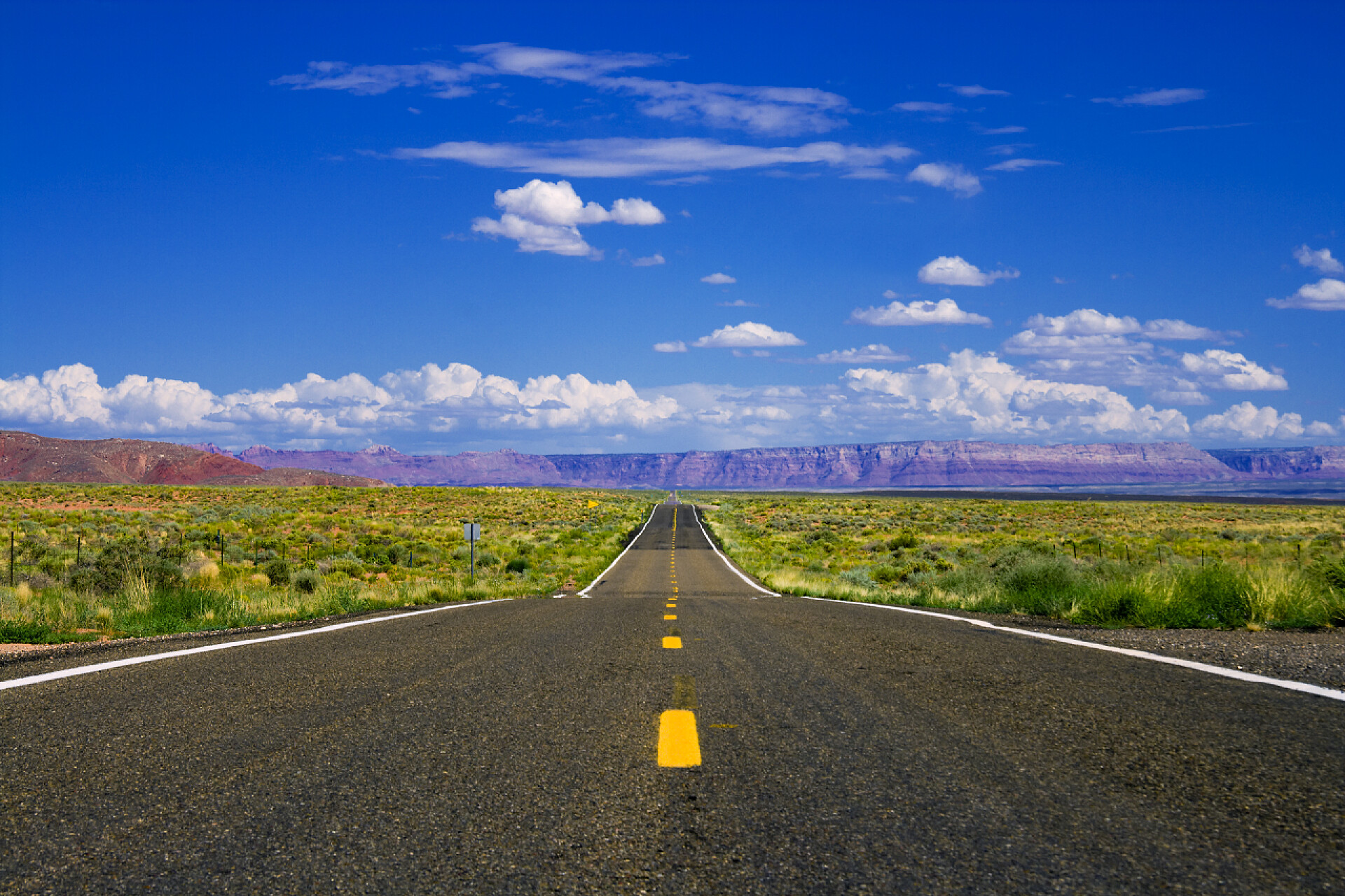 蓝天下空旷的田野中一条笔直向前的柏油马路沙漠公路