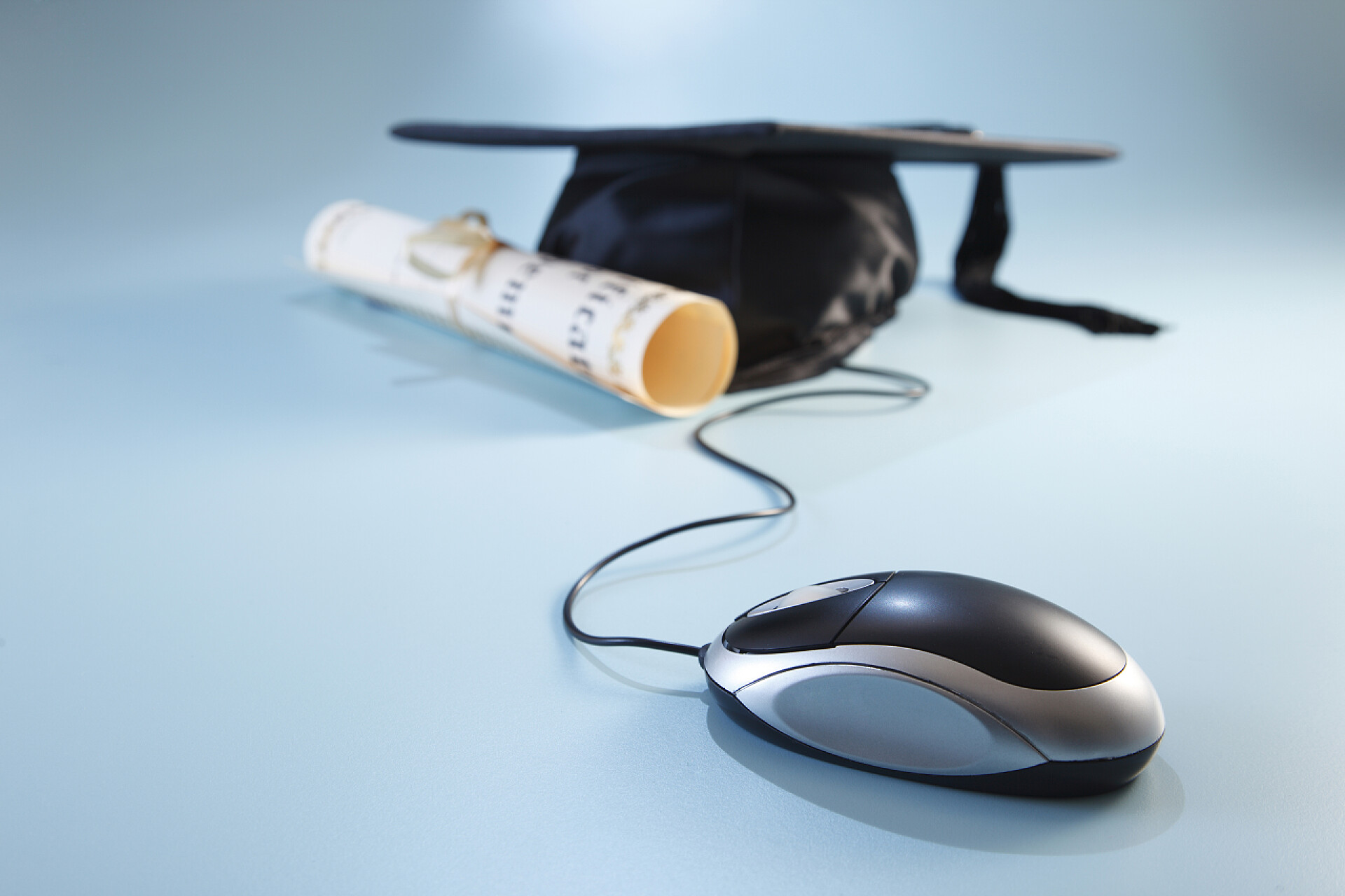在蓝色背景墙下的鼠标博士帽和毕业证书网上教育
