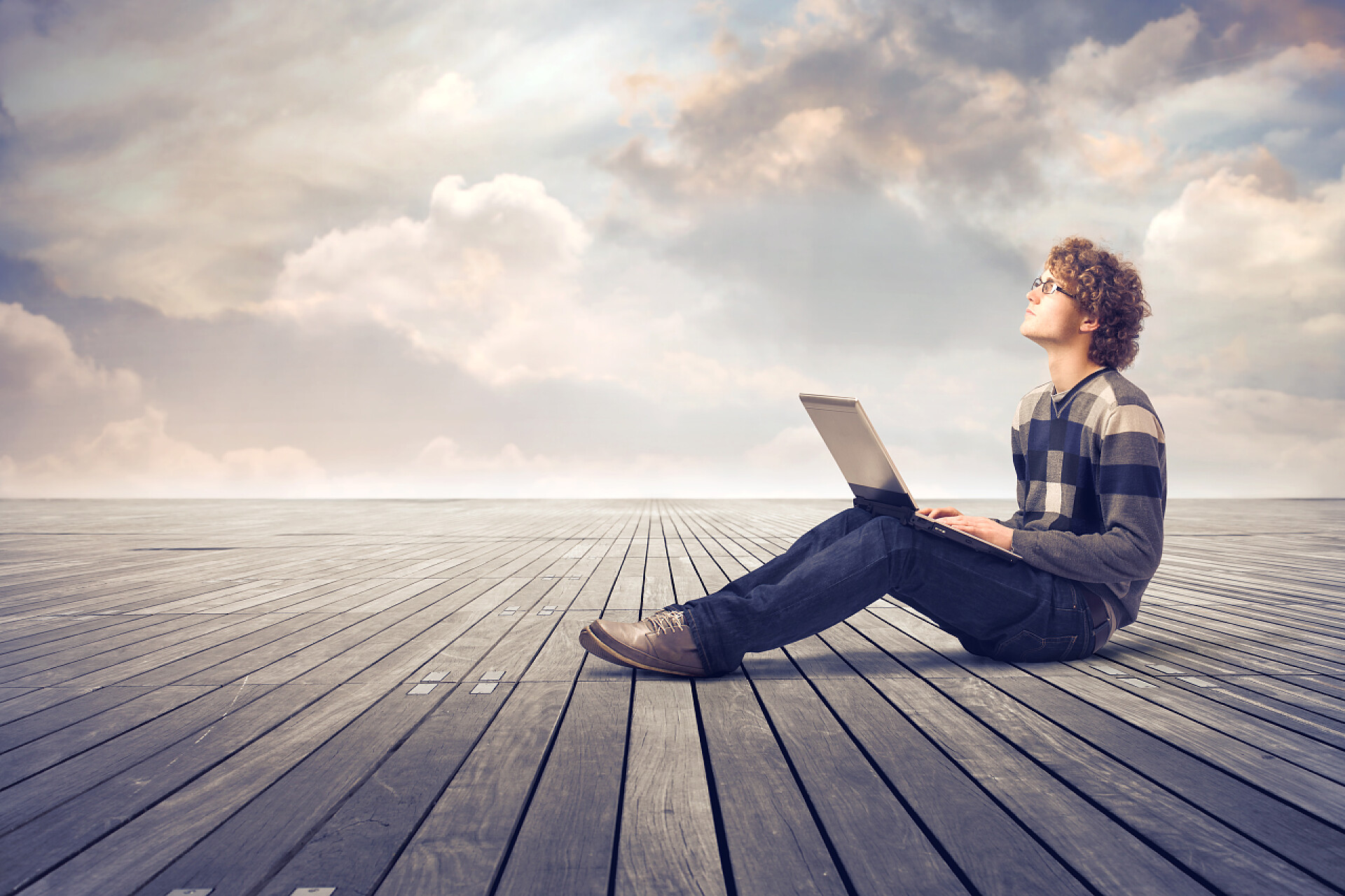 灰色天空下年轻男子坐在地板上使用一台笔记本电脑学习数码创意