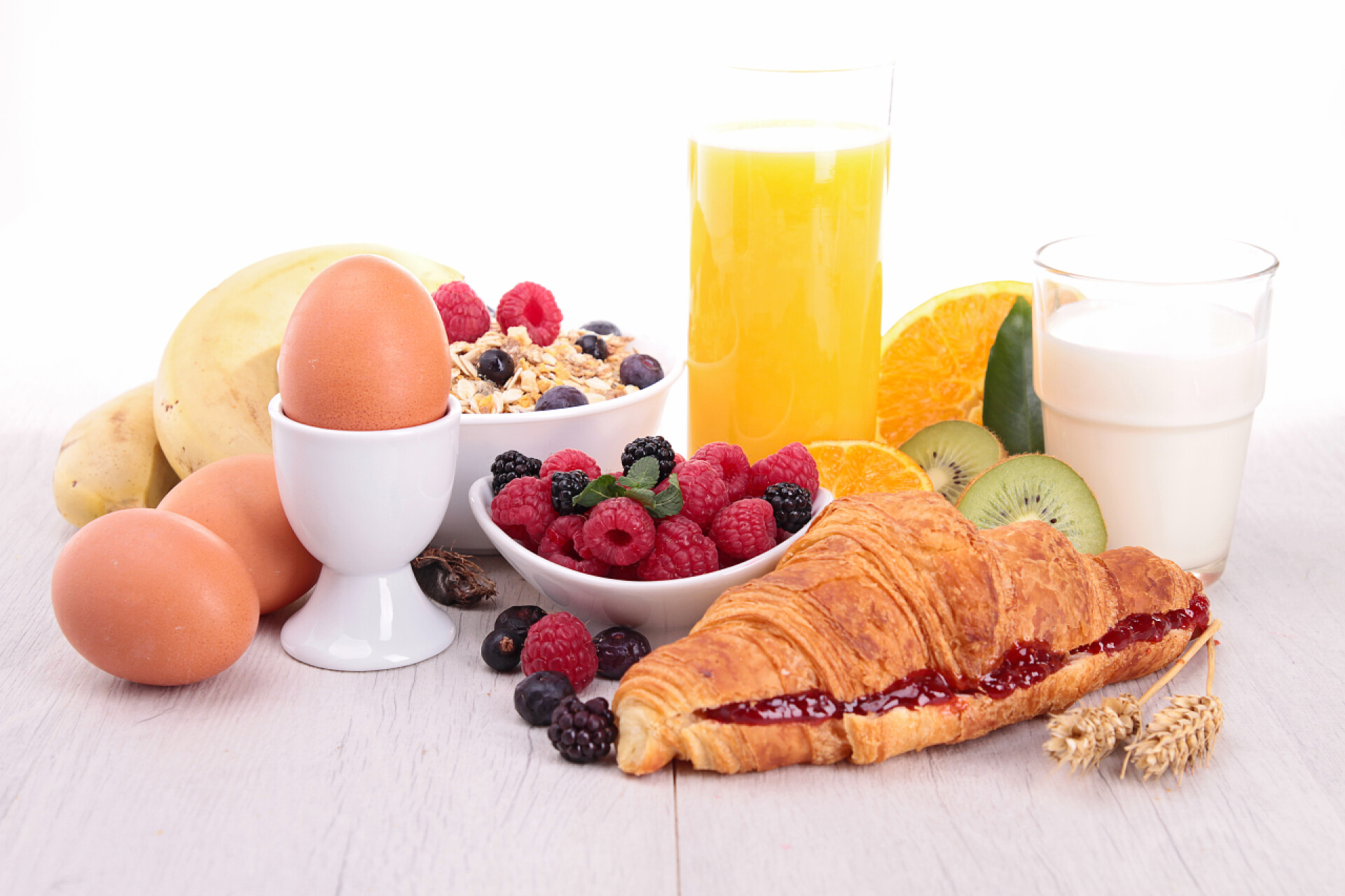 白色背景前丰富的早餐早餐鸡蛋、 牛角面包、 饮料和水果