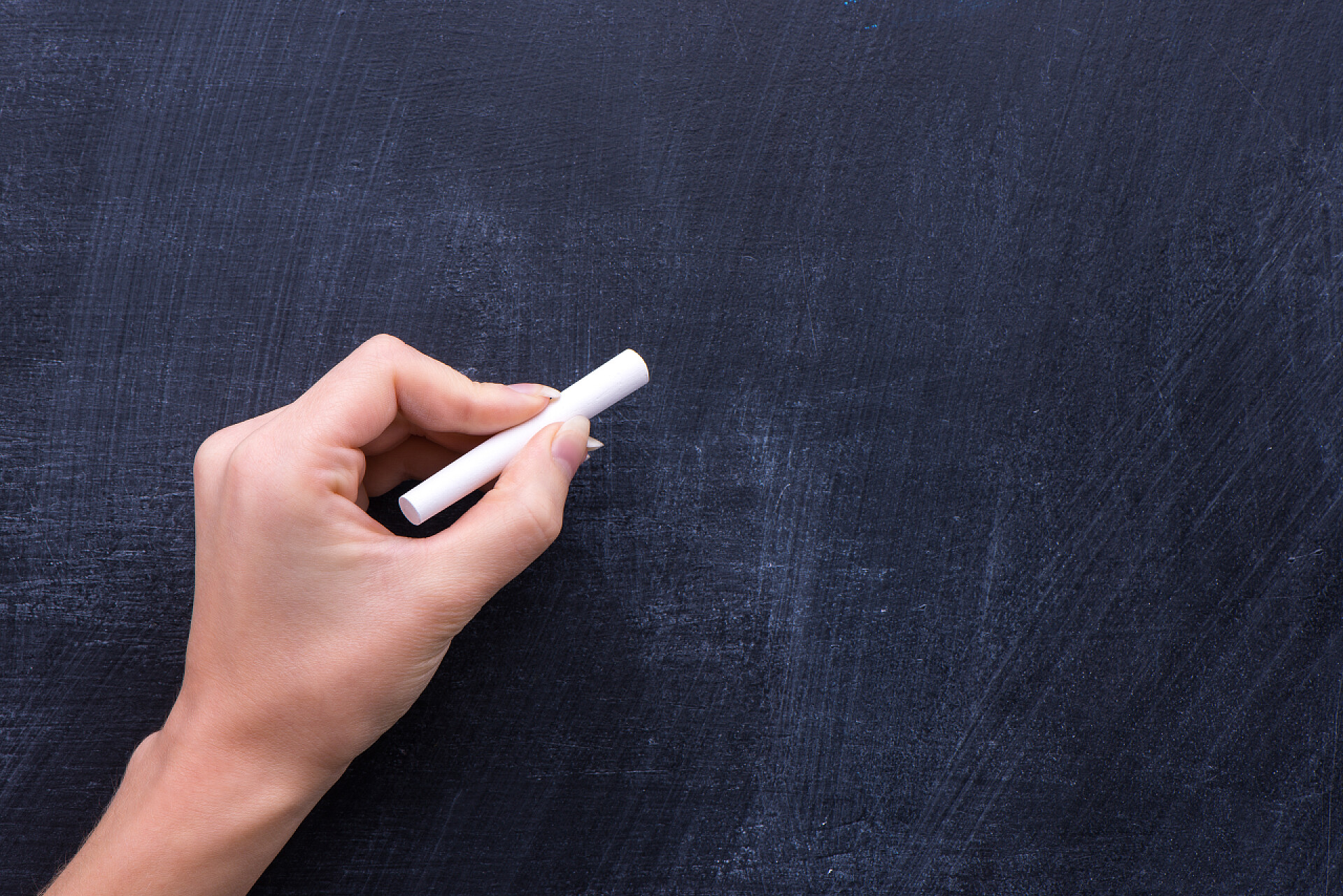 男人手拿着一支白色粉笔在黑板上写字Advirtisman 上黑板概念