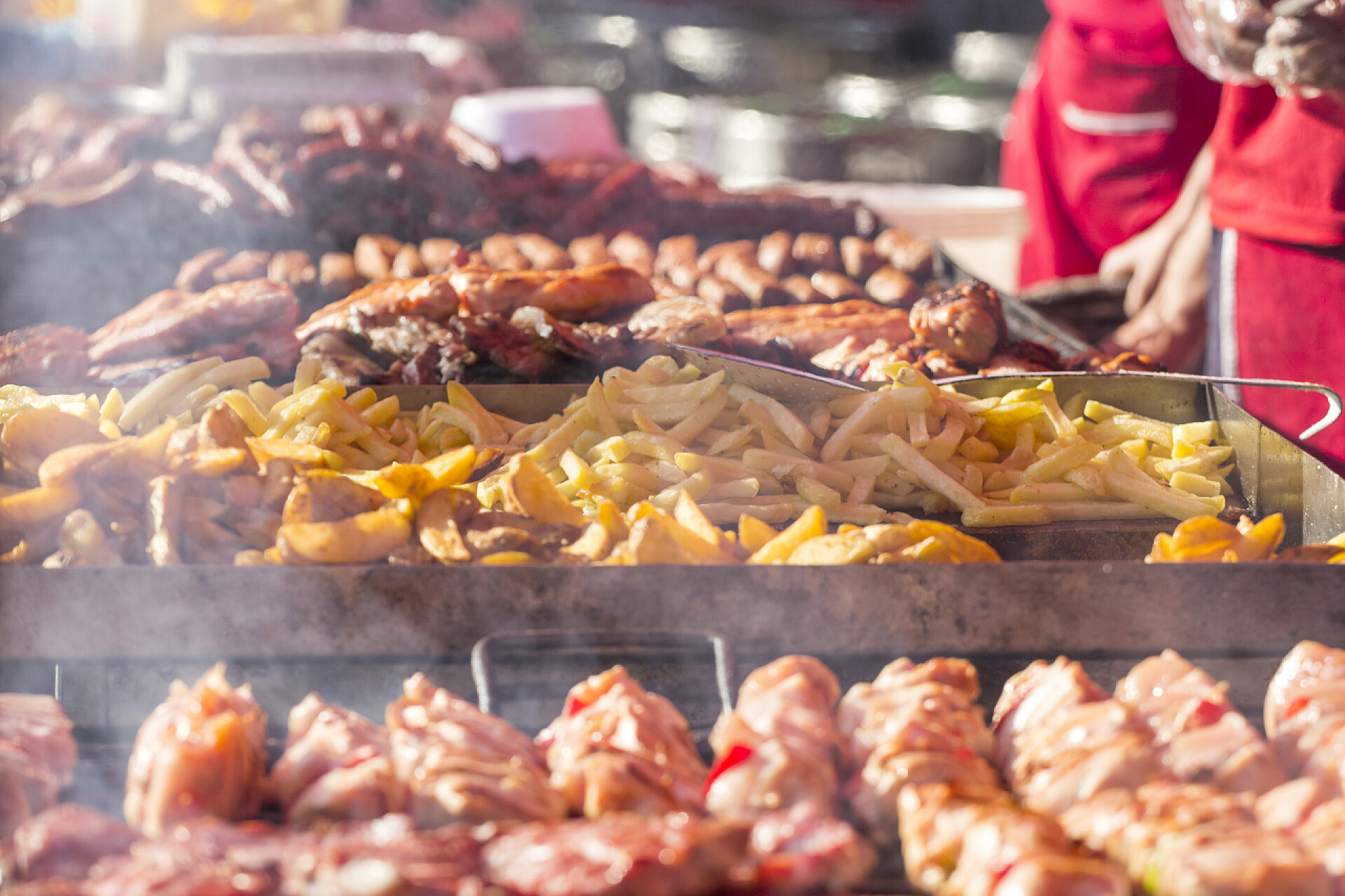 市场上烤架上的烤肉和薯条从烤架上烤的肉和香肠配烟和蒸汽不同种