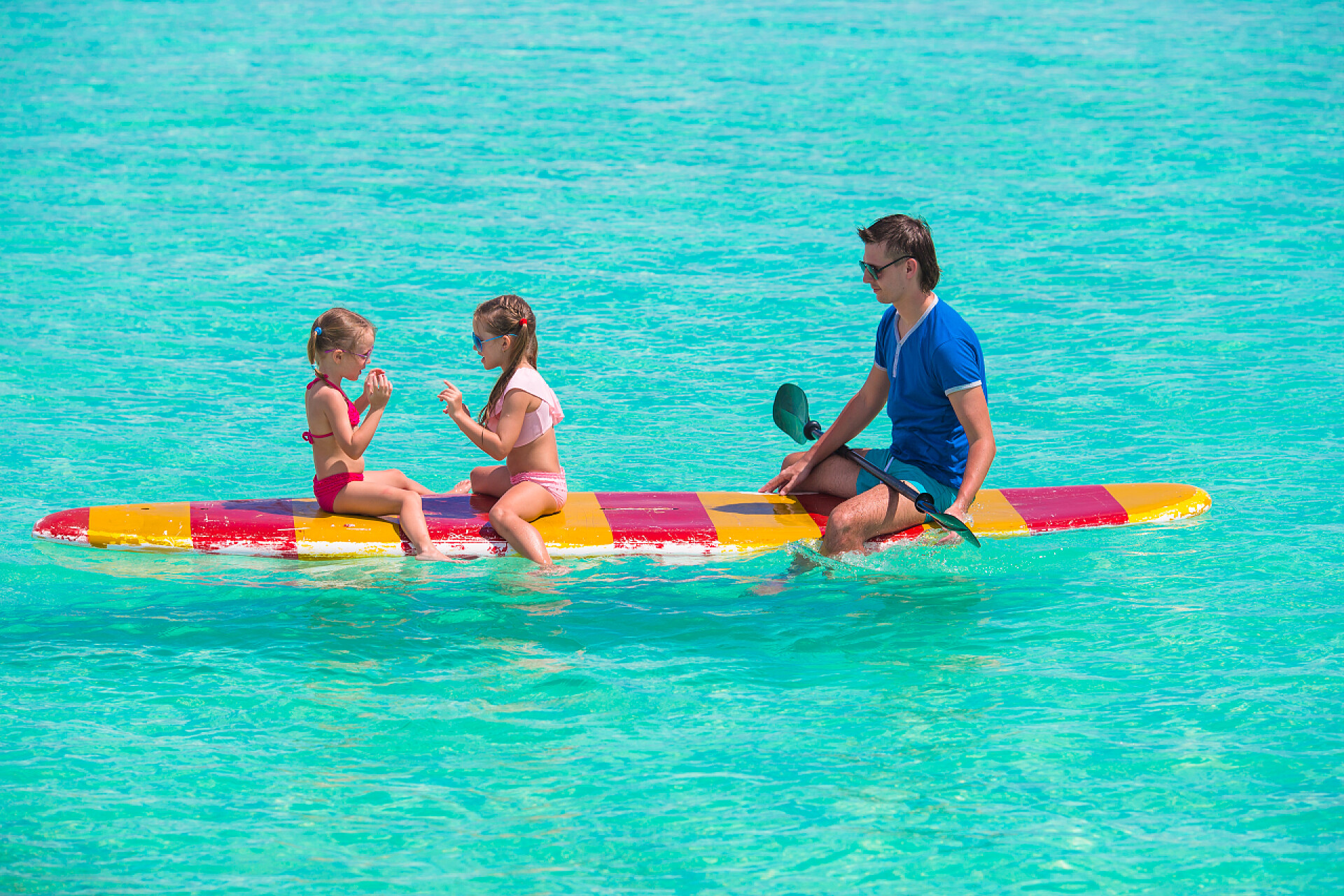 父亲带着孩子在冲浪板上玩耍暑假期间，小女孩和年轻爸爸在冲浪板上