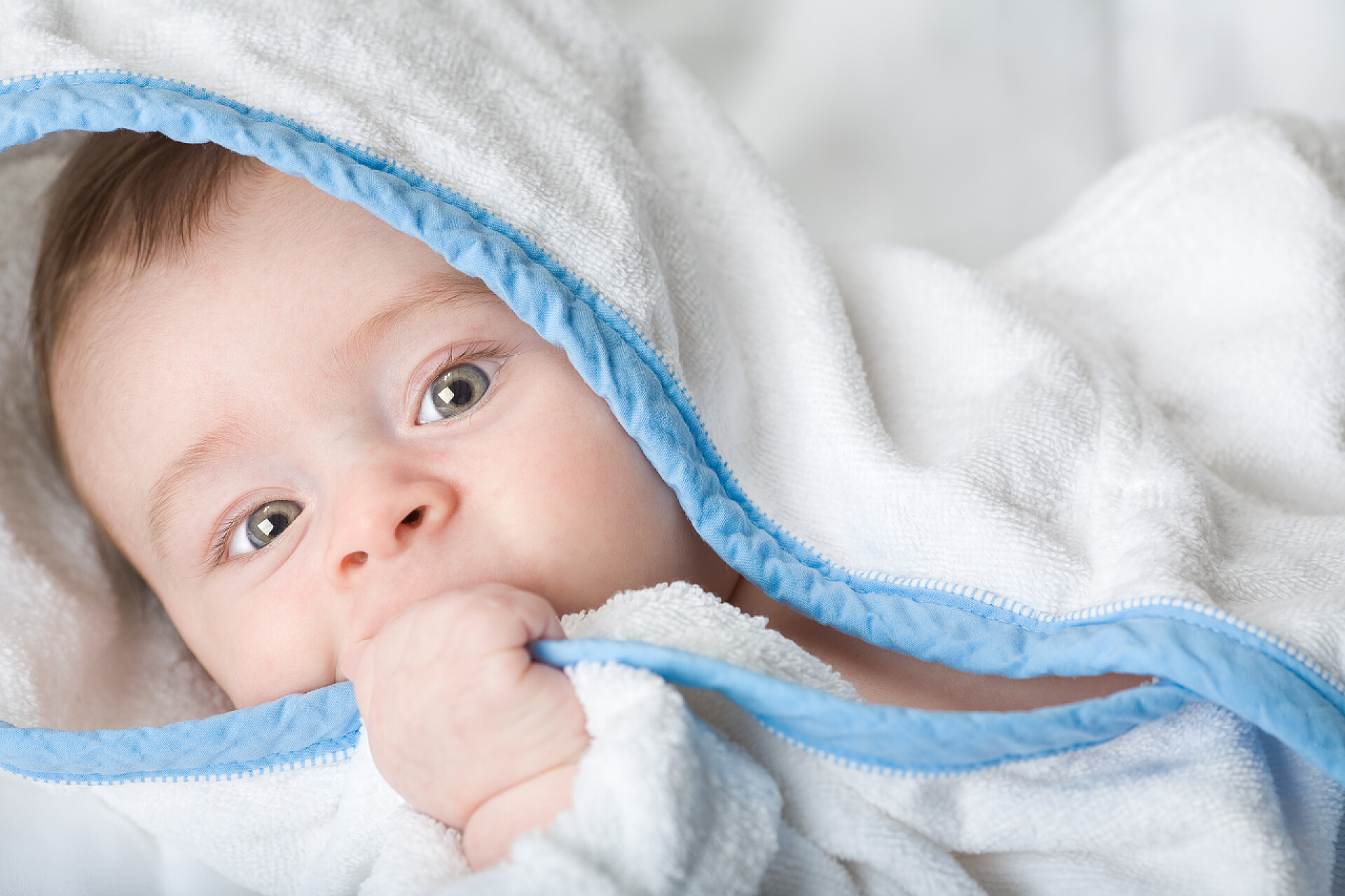 美丽的小宝宝在白色毛巾里咬手美丽的小宝宝，长着大眼睛在白色毛巾咬他的手