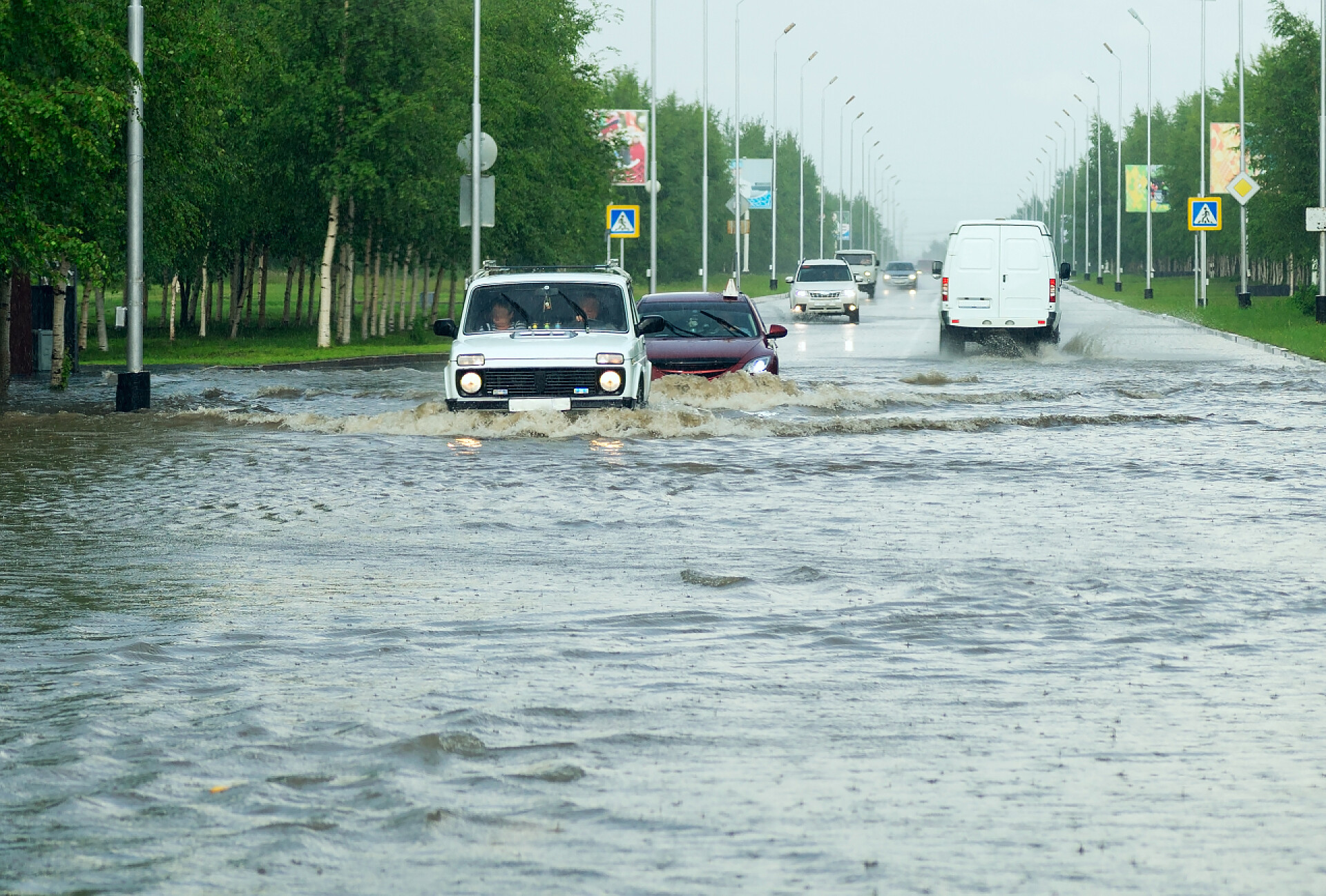 户外远景车辆在大雨中行驶道路安全配图汽车穿过城市街道上的一个巨大水坑.