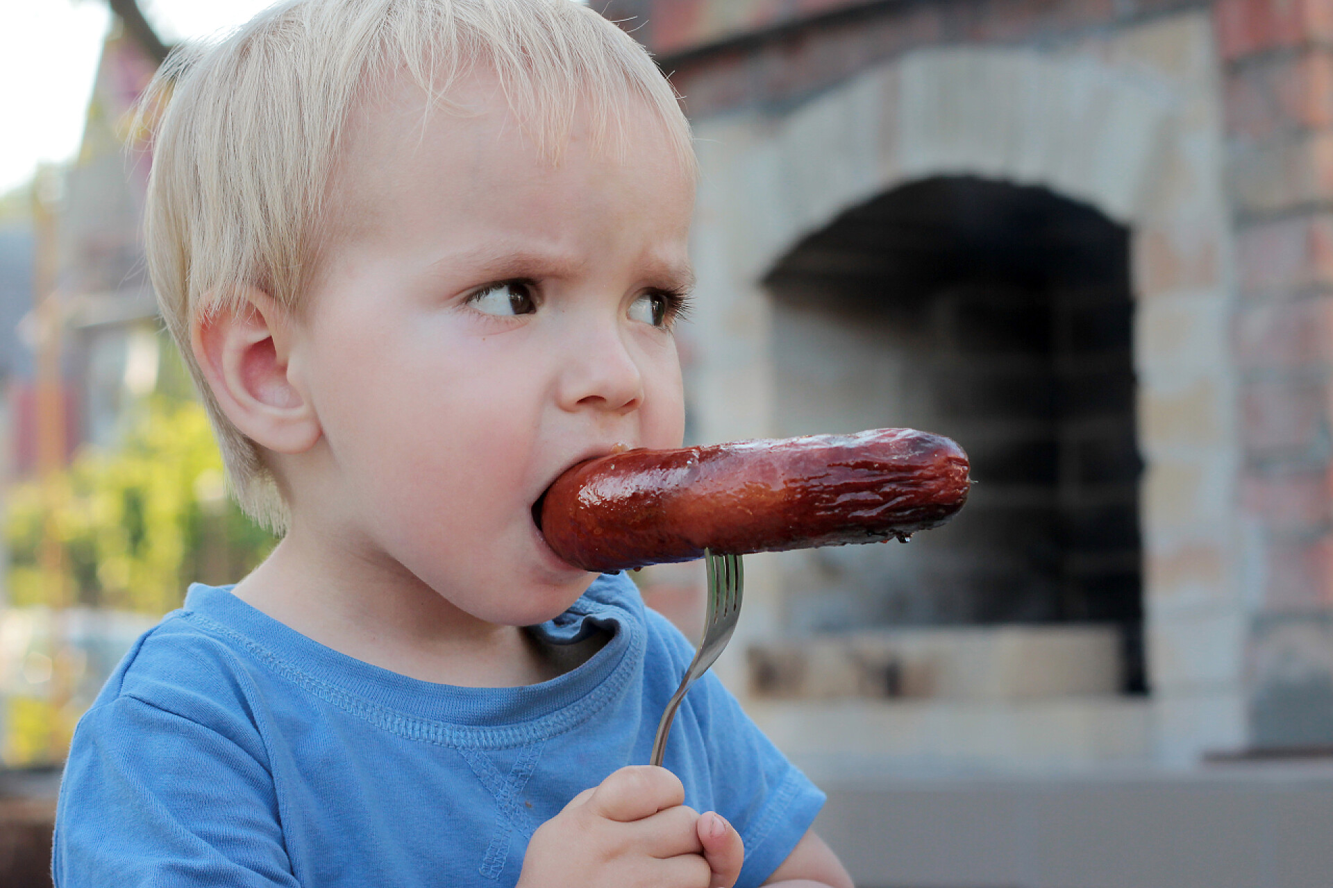 金发男孩咬着叉子上的香肠暑假的概念