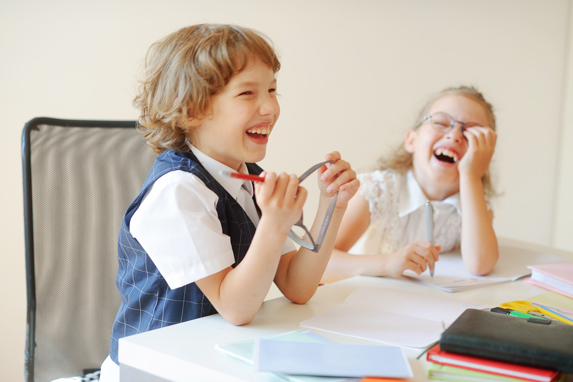 正在开心大笑的两个小孩有趣的学童，男孩和女孩，坐在一张桌子.