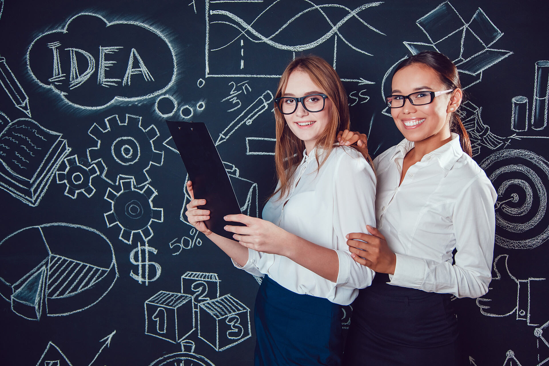 两个女老师站在黑板前欧洲人和亚洲商界女性戴着眼镜，站在一个黑暗的背景