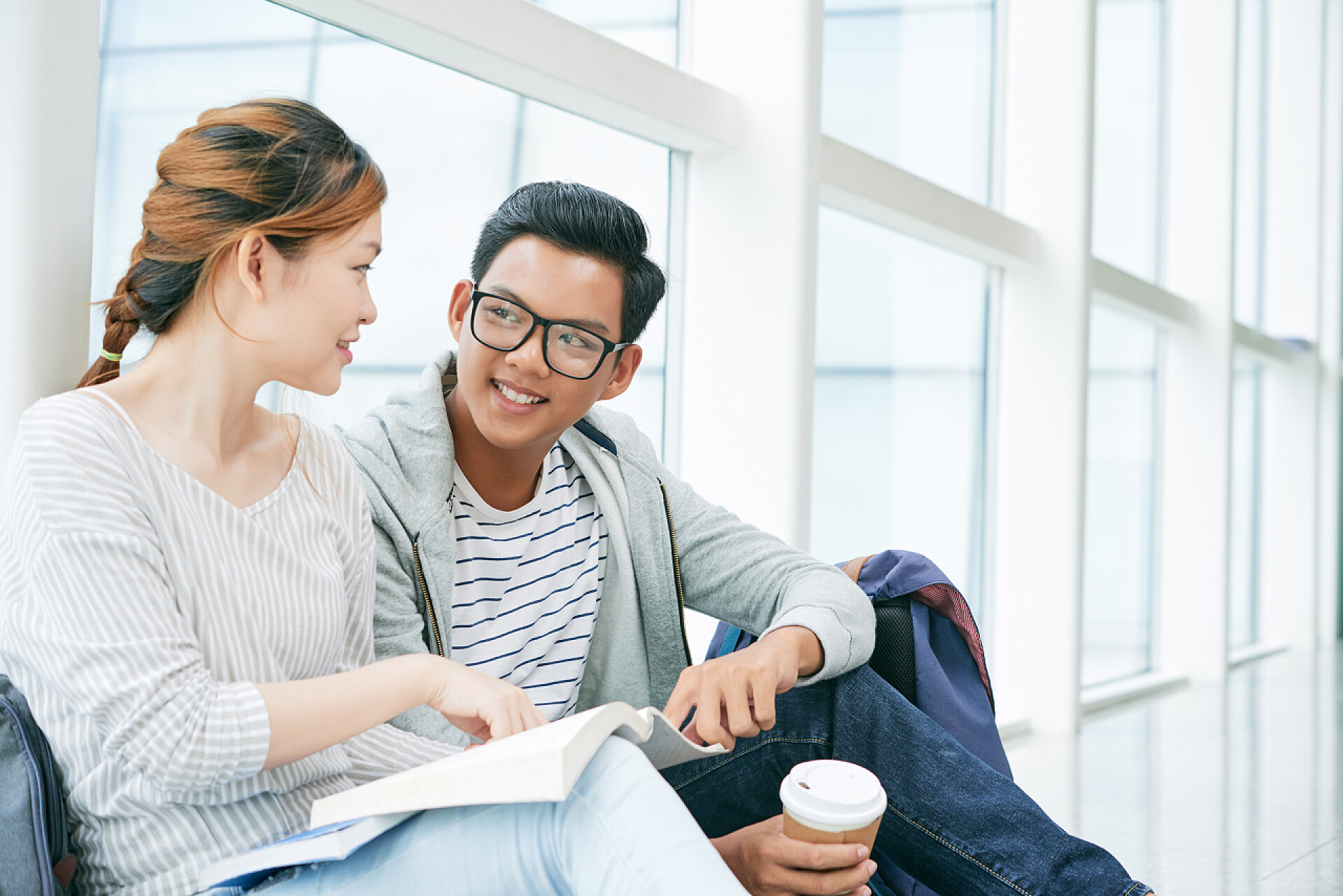两个亚洲学生坐在窗口讨论学术同学们在讨论坐在窗户